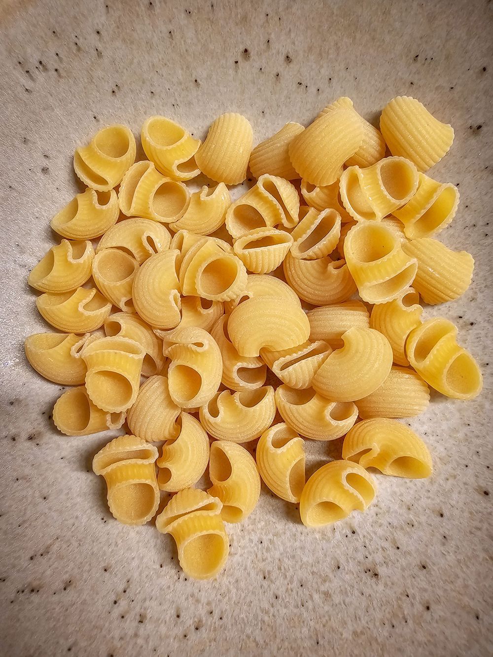 A sequence of images showing scattered uncooked shell pasta noodles arranged in different patterns on a textured surface.