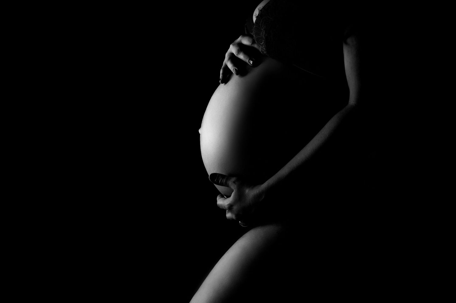 Artistic silhouette of pregnant belly against dark background.