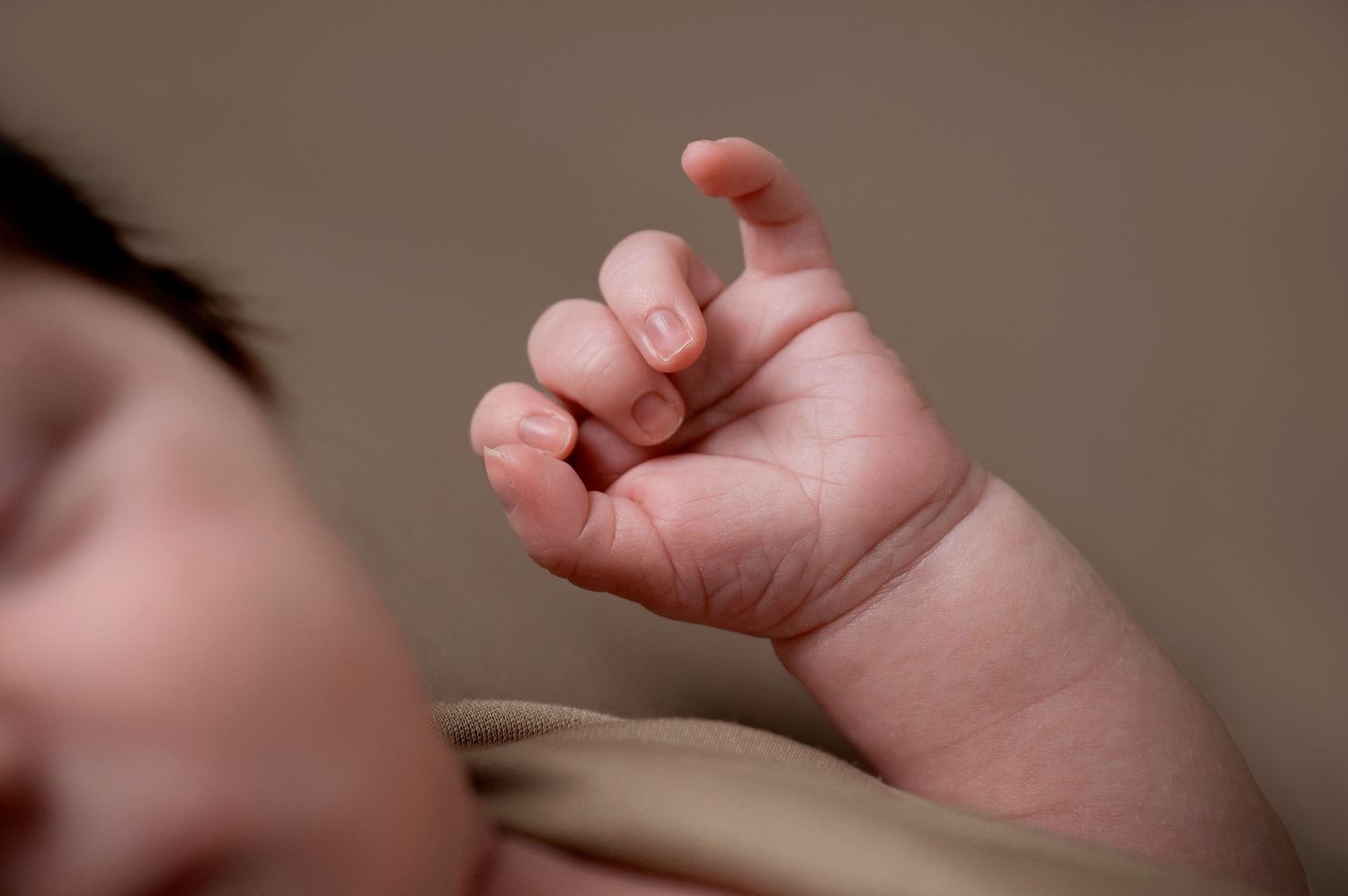 Close-up detail of a tiny newborn hand with curled fingers.