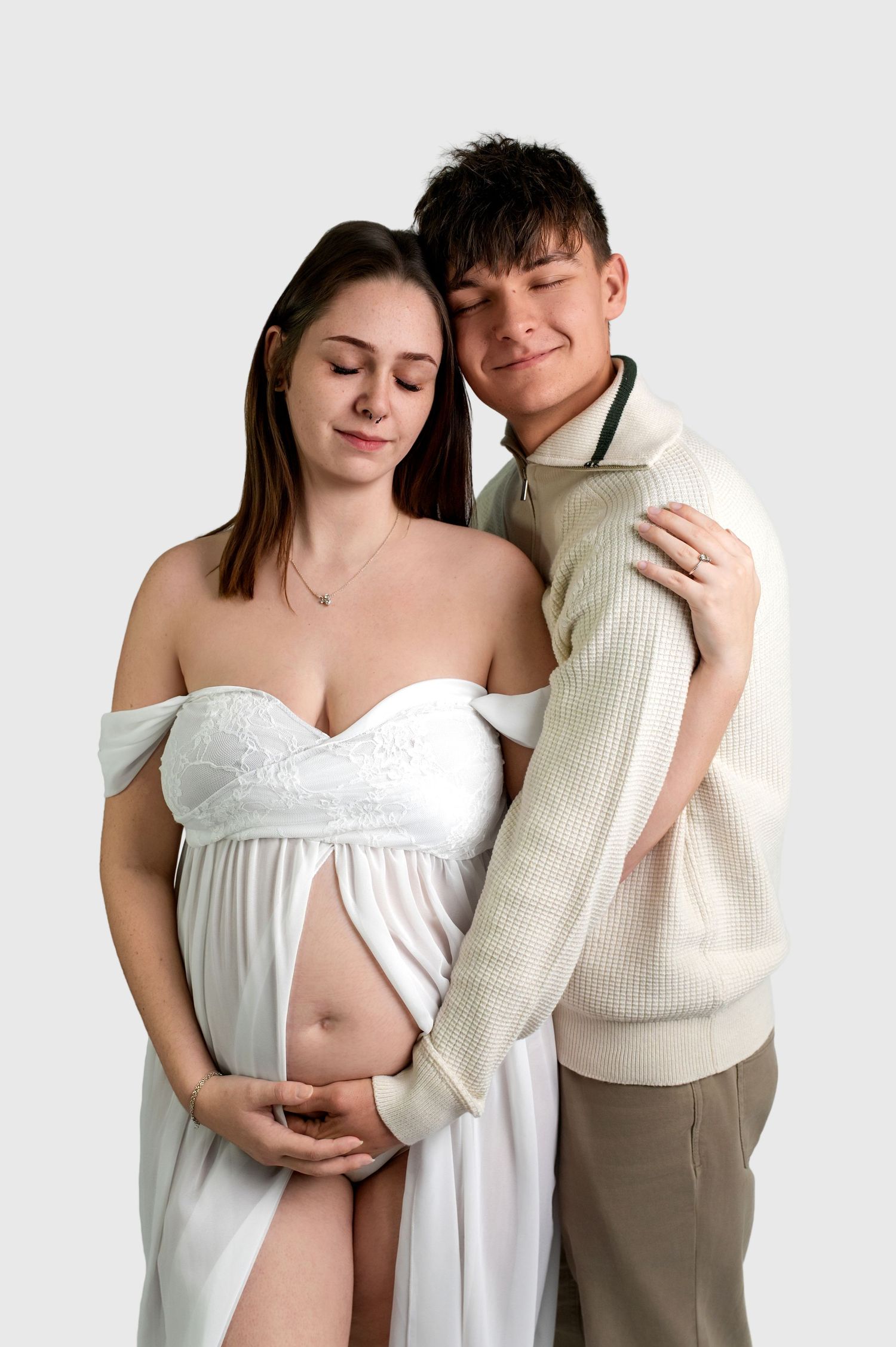 A tender maternity photo featuring an expecting couple in white and beige against a light background.