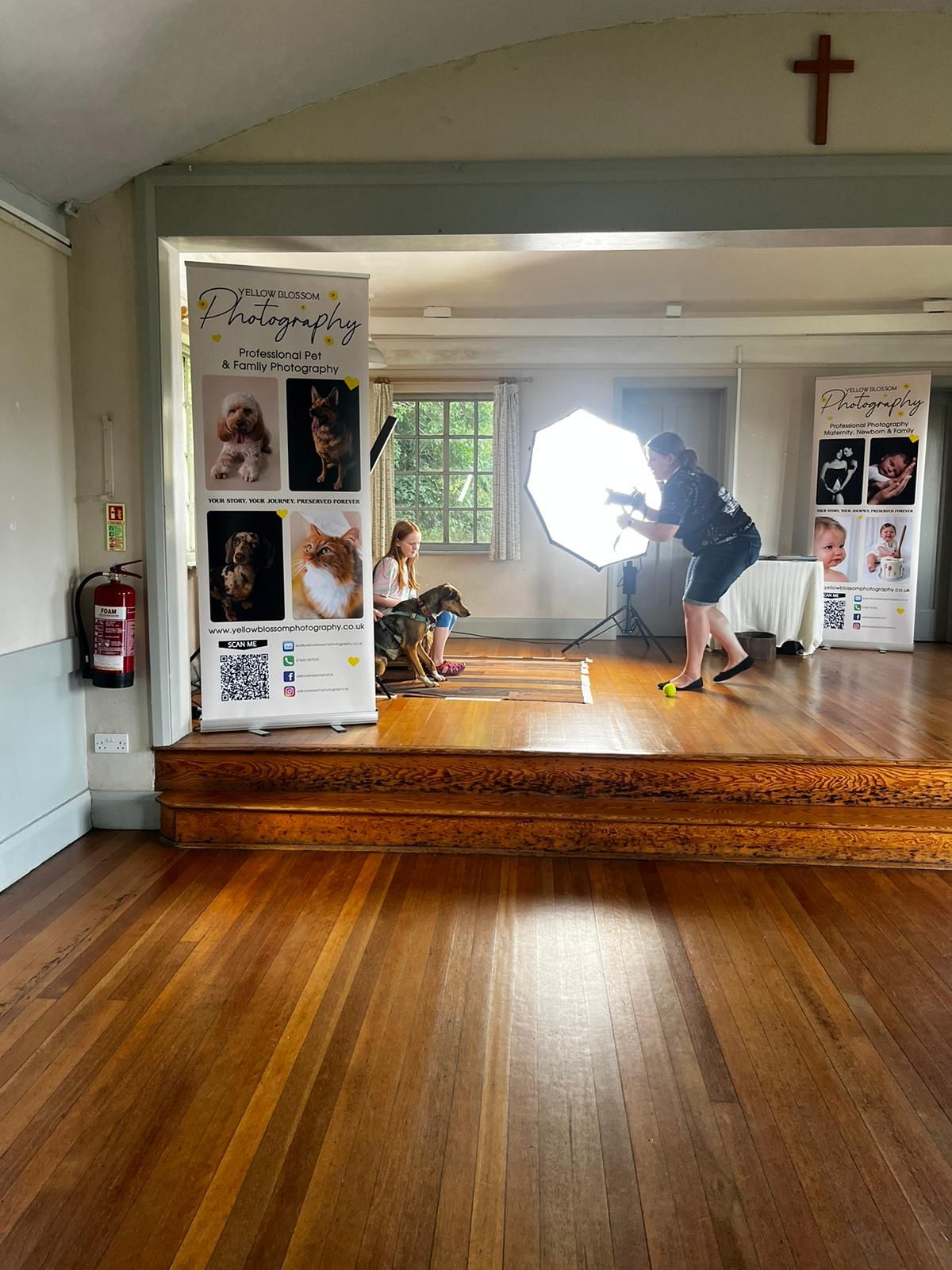 Photographer with studio lighting photographing a dog at a photography studio setup inside a wooden-floored hall.