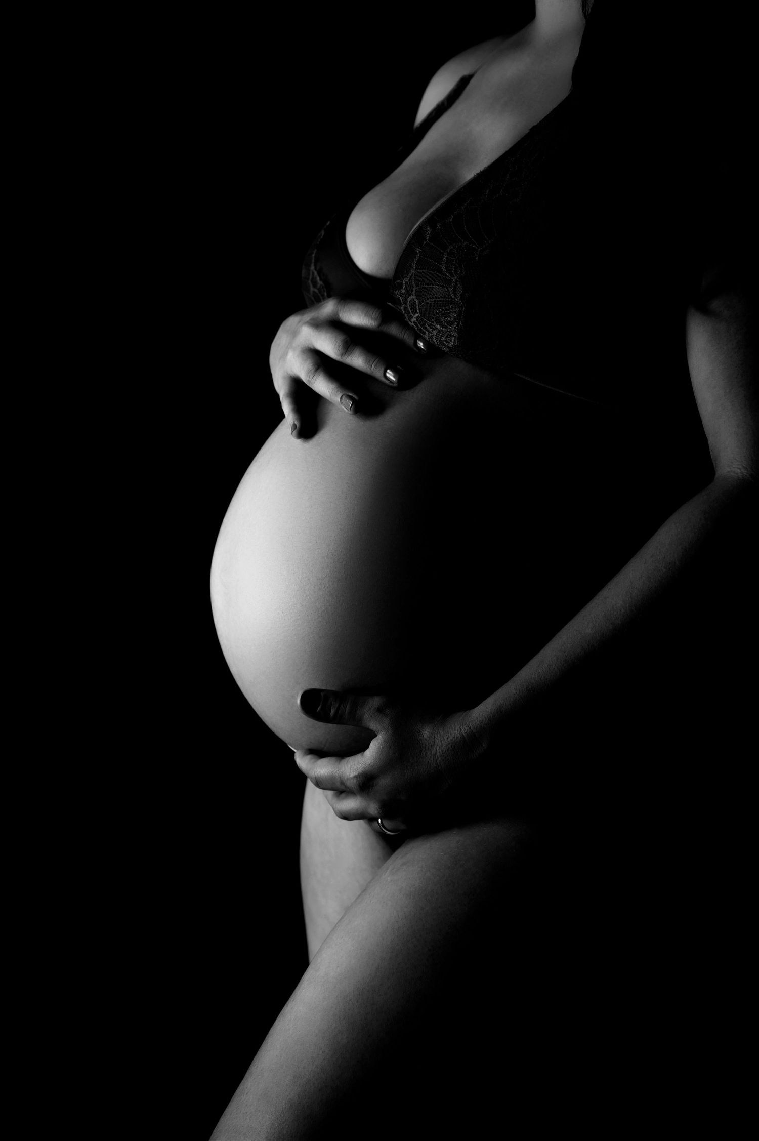 Dramatic black and white photo of hands cradling pregnant belly in darkness.