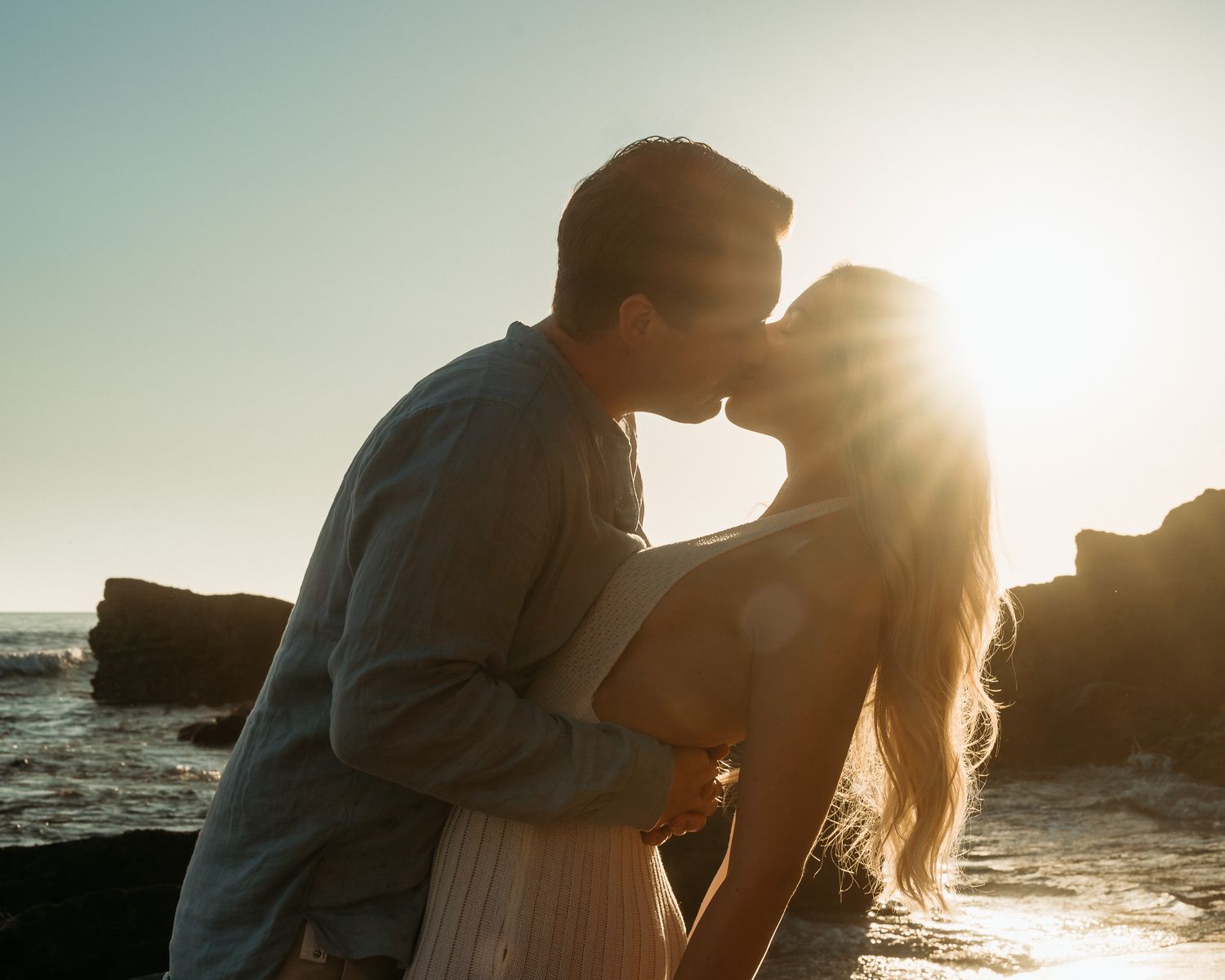 A couple embraces in a kiss in a silhouette against a golden sunset on the beach with ocean waves in the background. Mariano Alvarez Photo