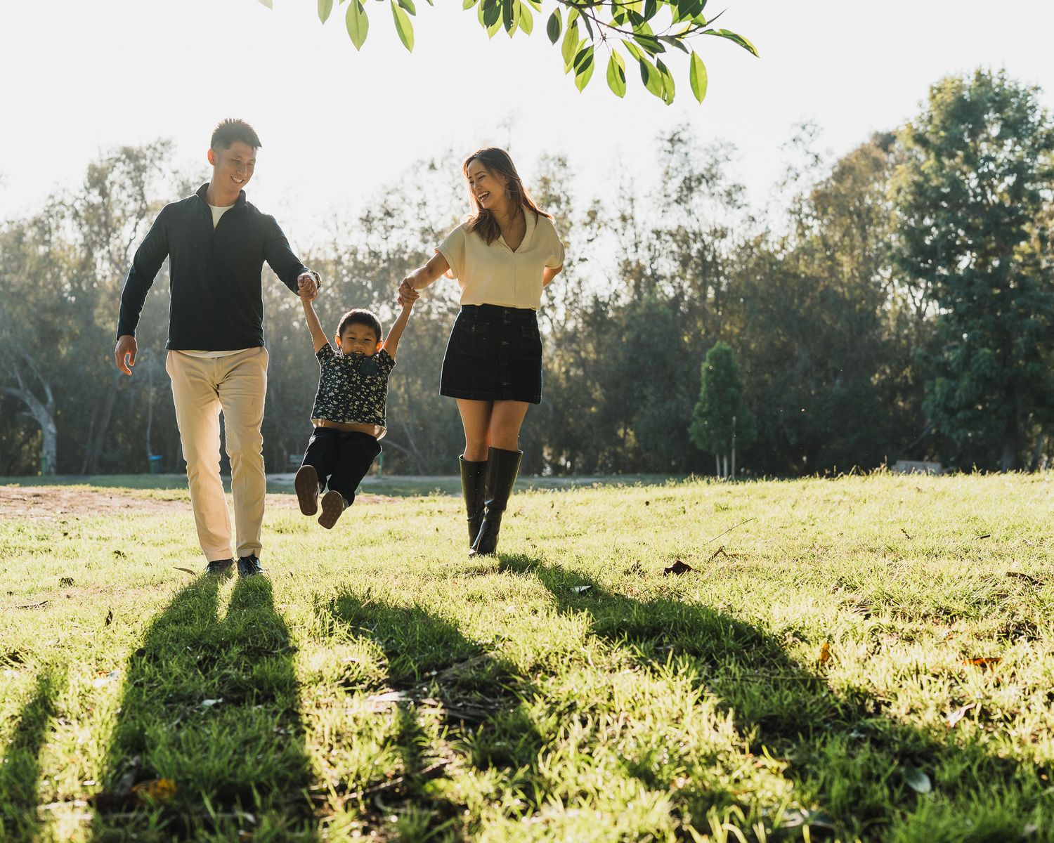 Family walking together through a sunlit meadow at golden hour as sun streams through trees.