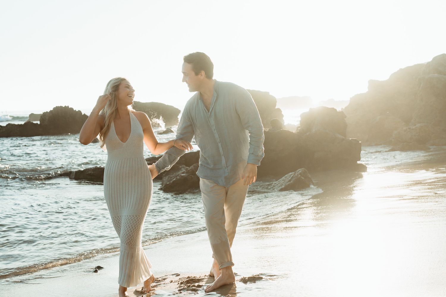 Couple walking hand in hand along a beautiful beach shore during golden hour.