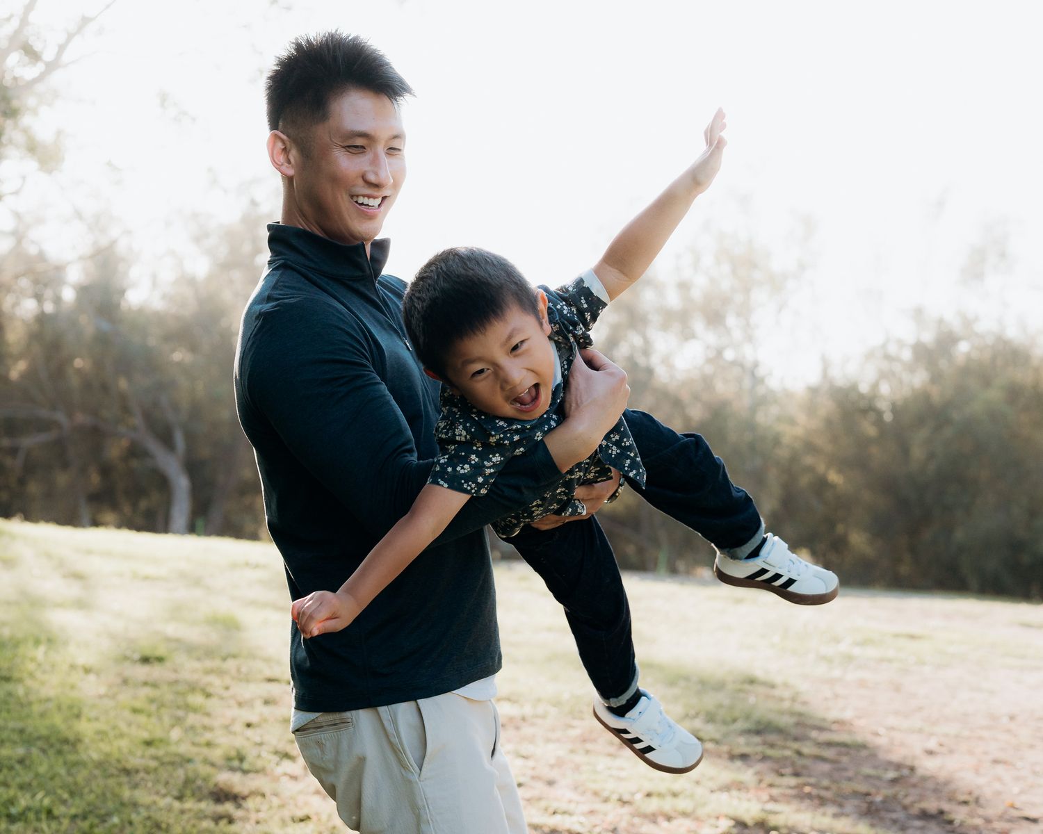 A joyful parent and child share playful moments together outdoors during a sunny afternoon photo session.