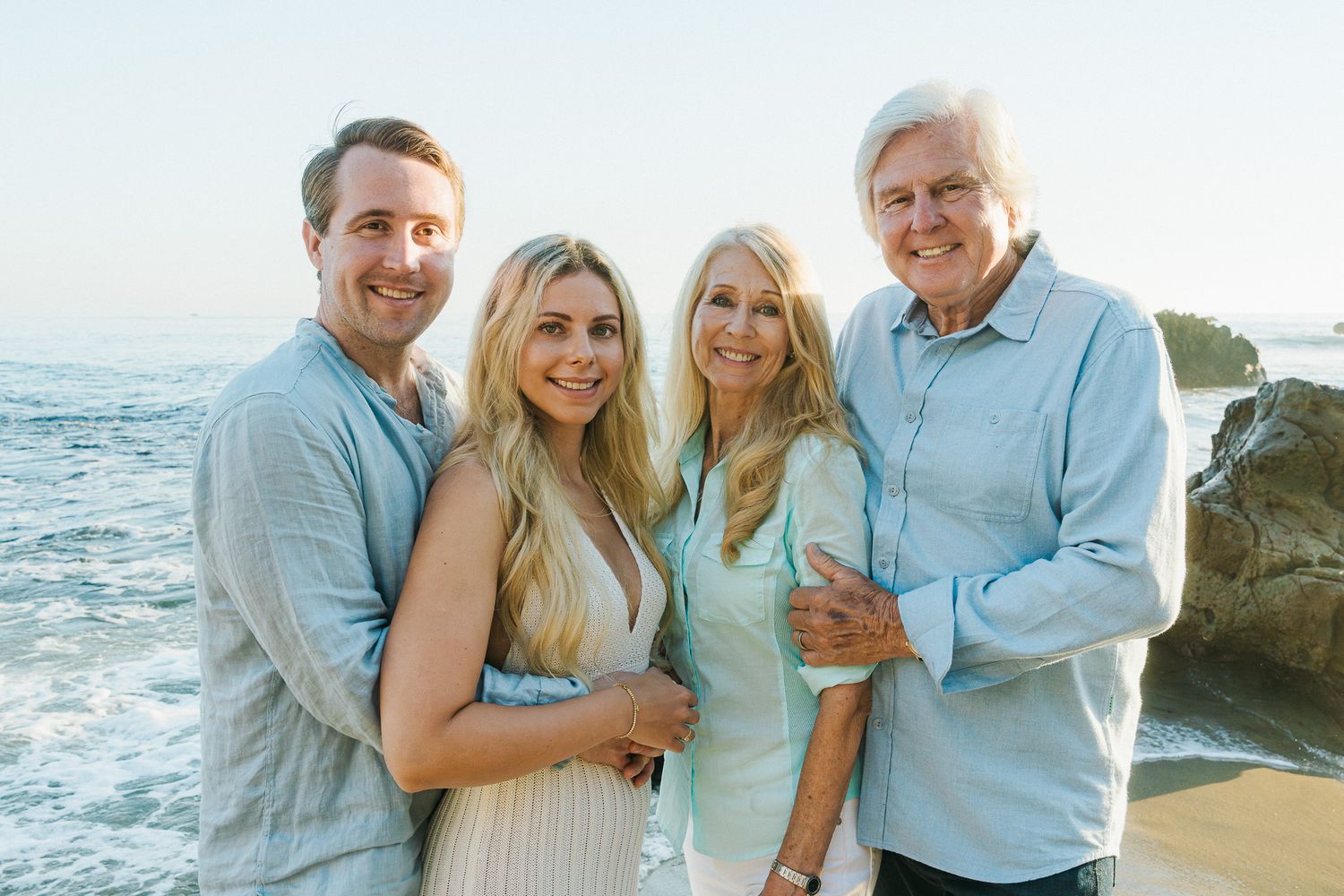 Family poses together on rocky beach at sunset in coordinating blue and mint outfits.