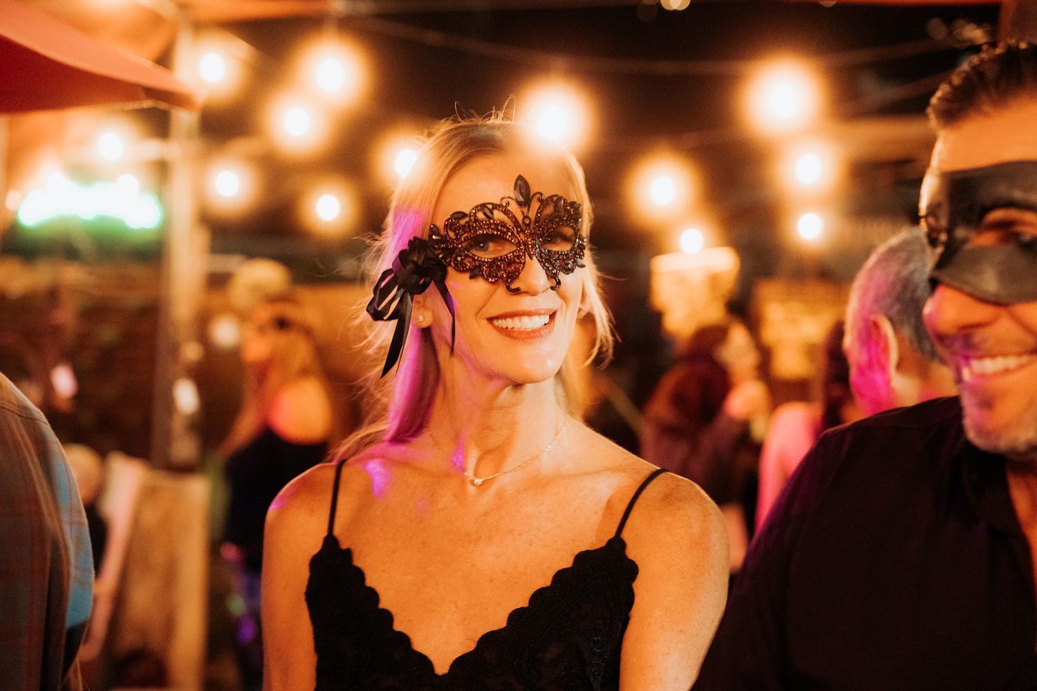 A group of people dancing and celebrating at an evening wedding reception under warm string lights.