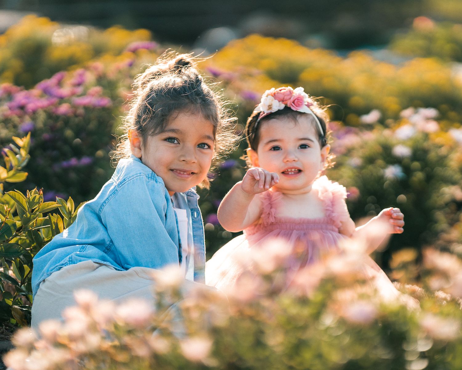 Children play in a blooming garden filled with colorful flowers during golden hour.