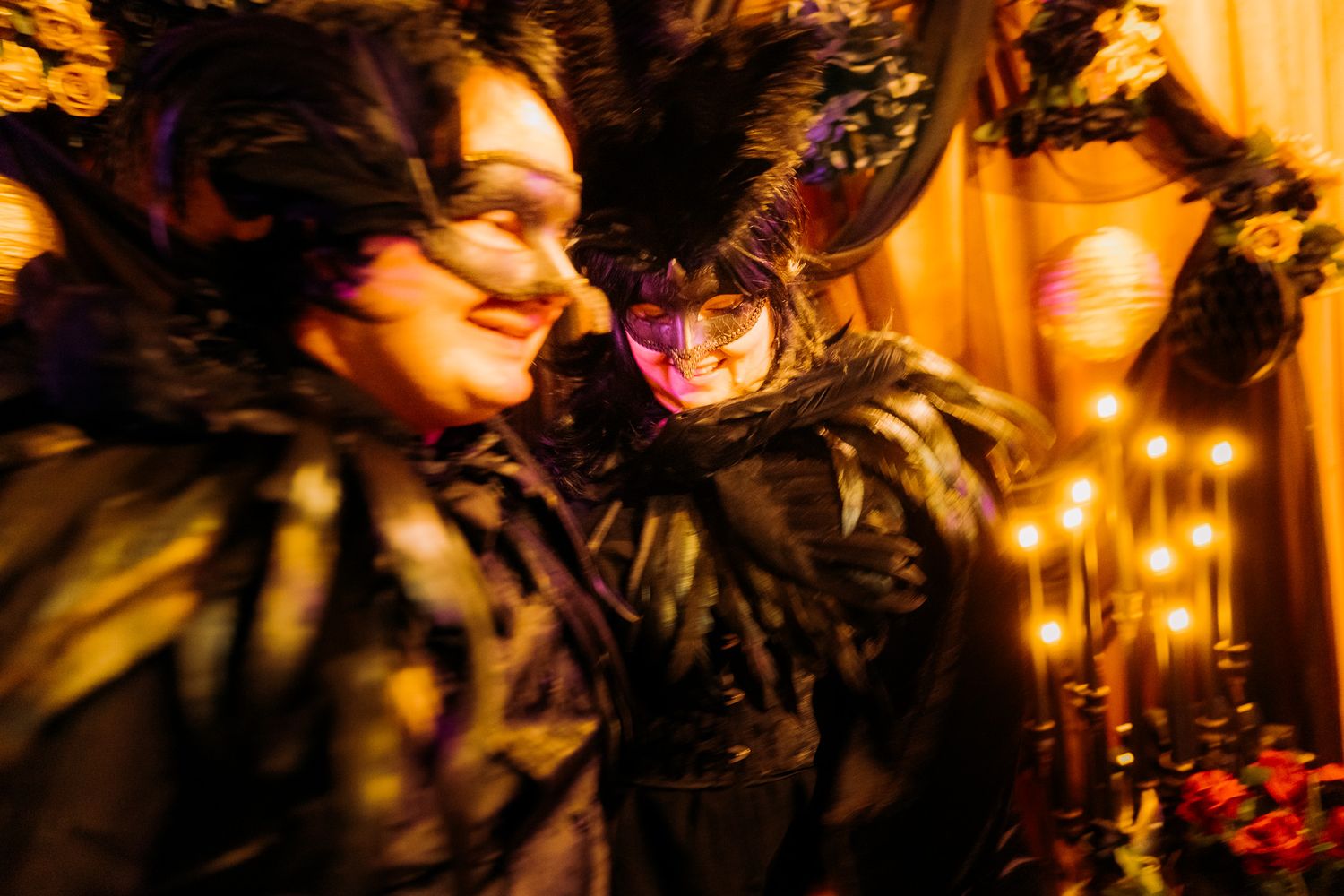 Guests wearing ornate masquerade masks celebrate at an elegant party with warm golden lighting and decorative elements.