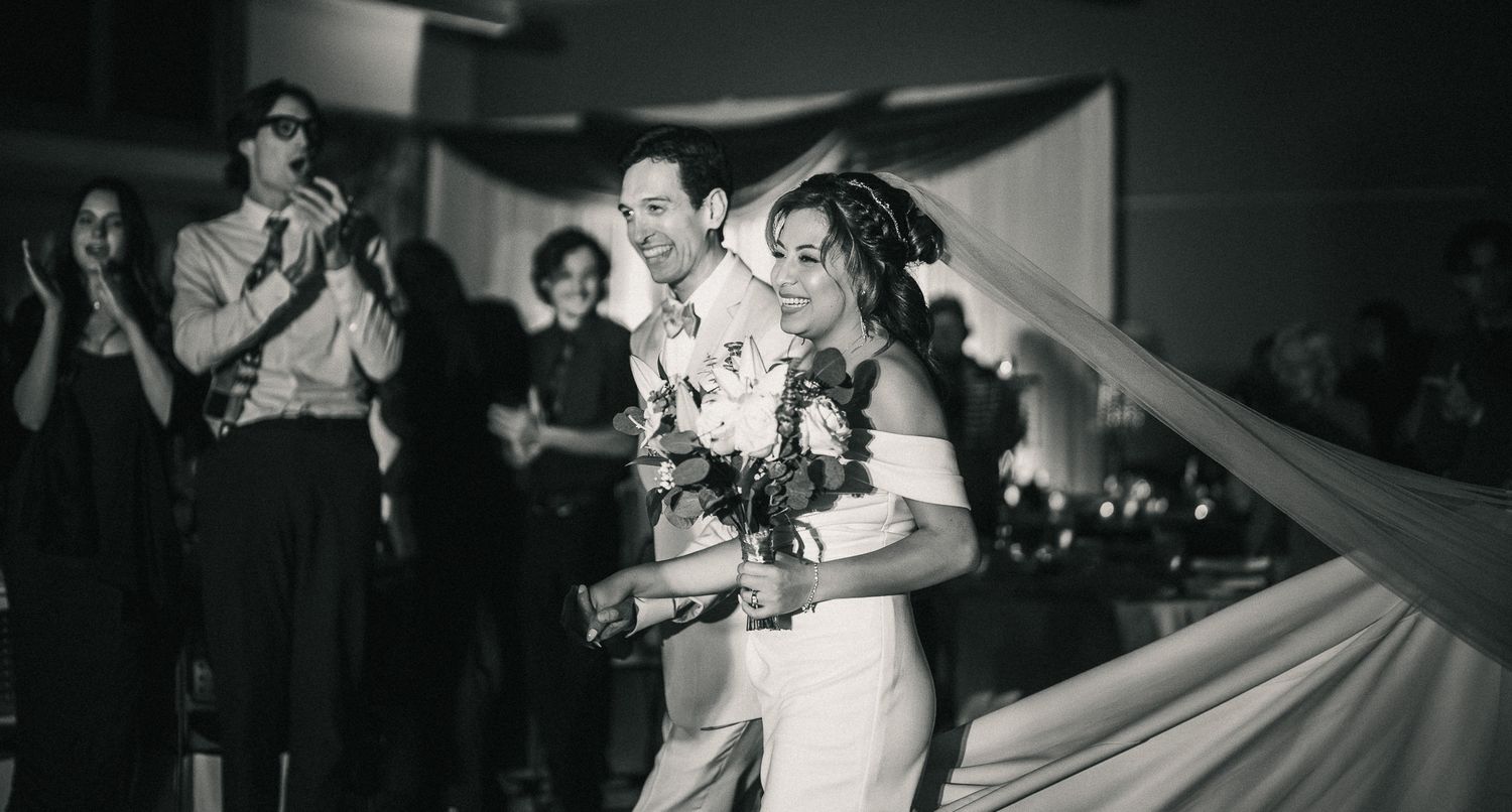 A couple dances together at a wedding reception while guests watch in a dimly lit venue.