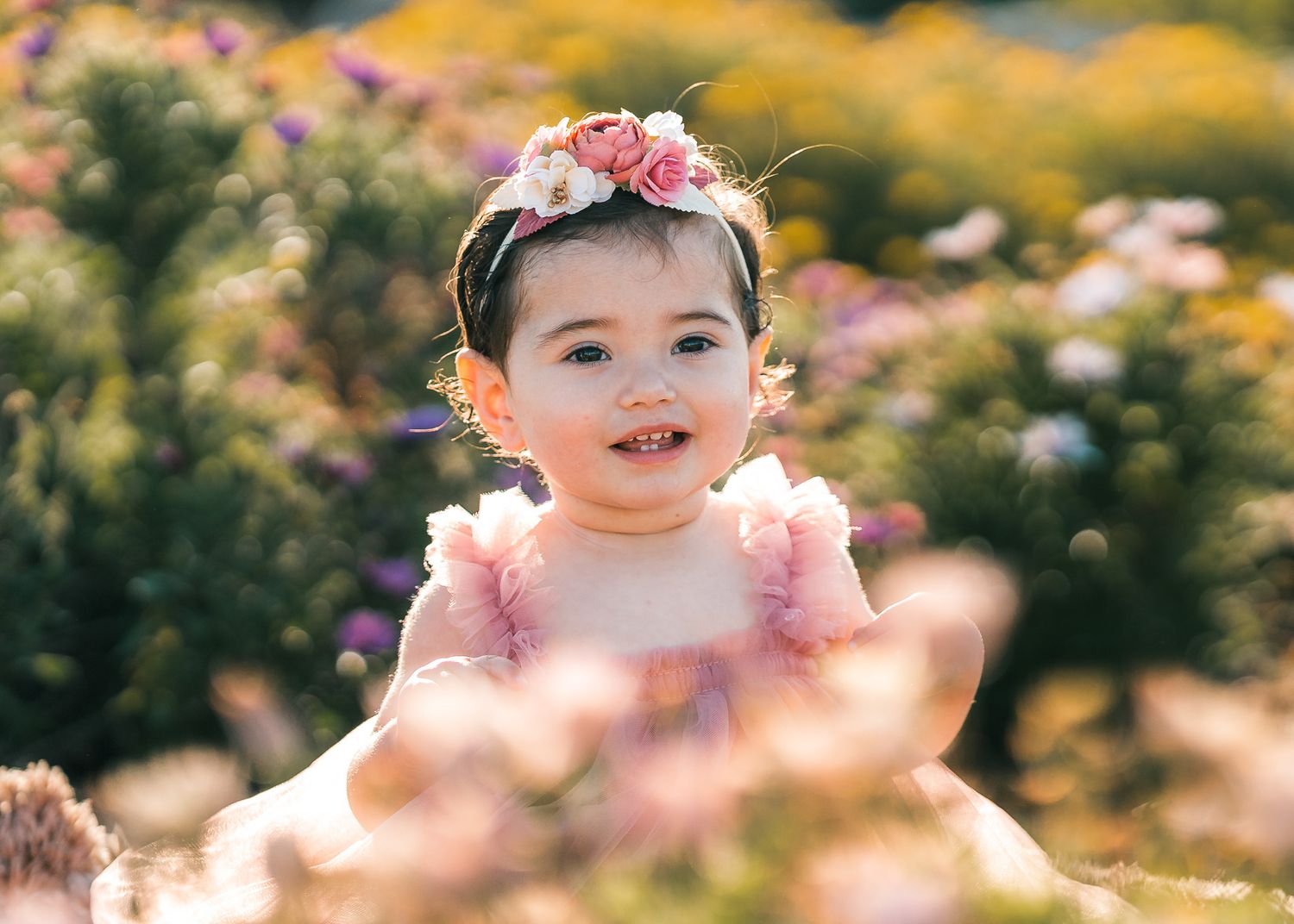 Sunlit garden scene with pink and yellow flowers framing a joyful outdoor photography session.