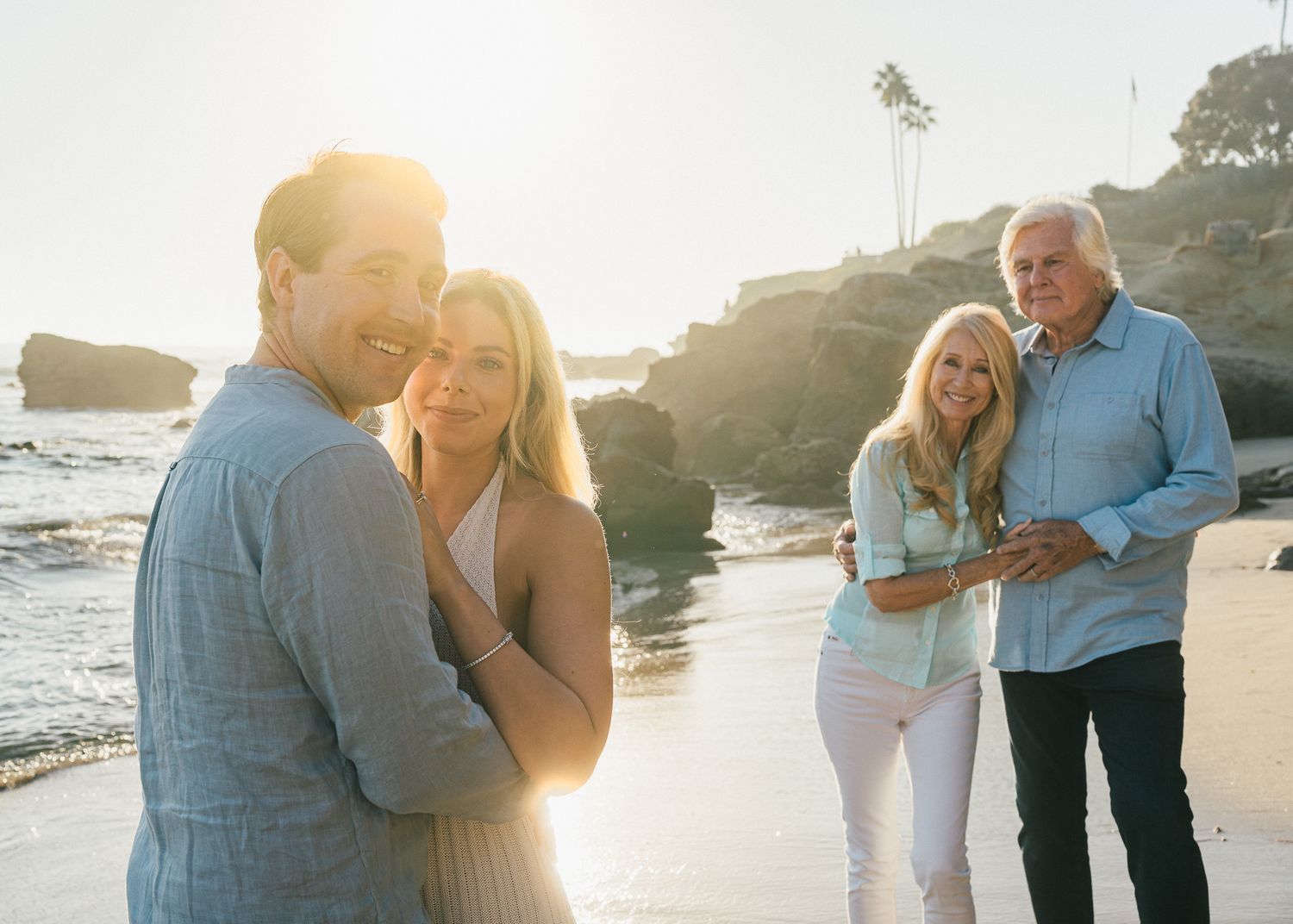 Romantic couple embraces on a sunlit beach during golden hour as waves crash on the shore in the background.