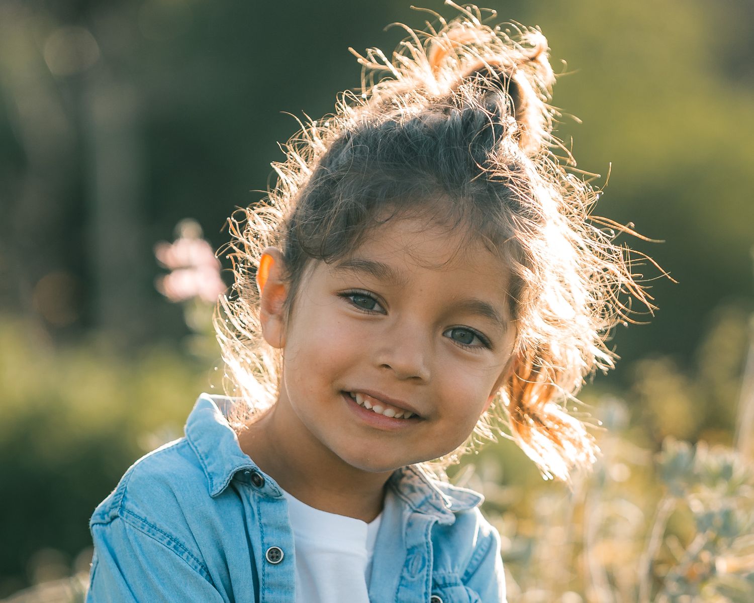 Child smiling with backlit hair glowing in golden sunlight outdoors.