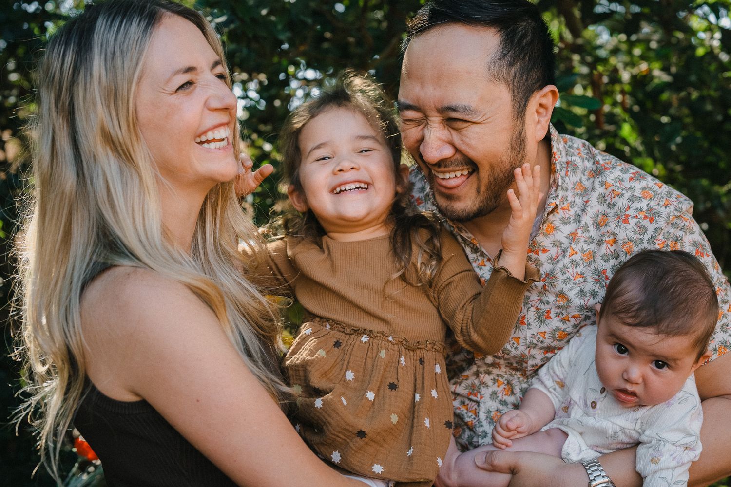 Happy family of four sharing joyful laughter together outdoors in a garden setting.