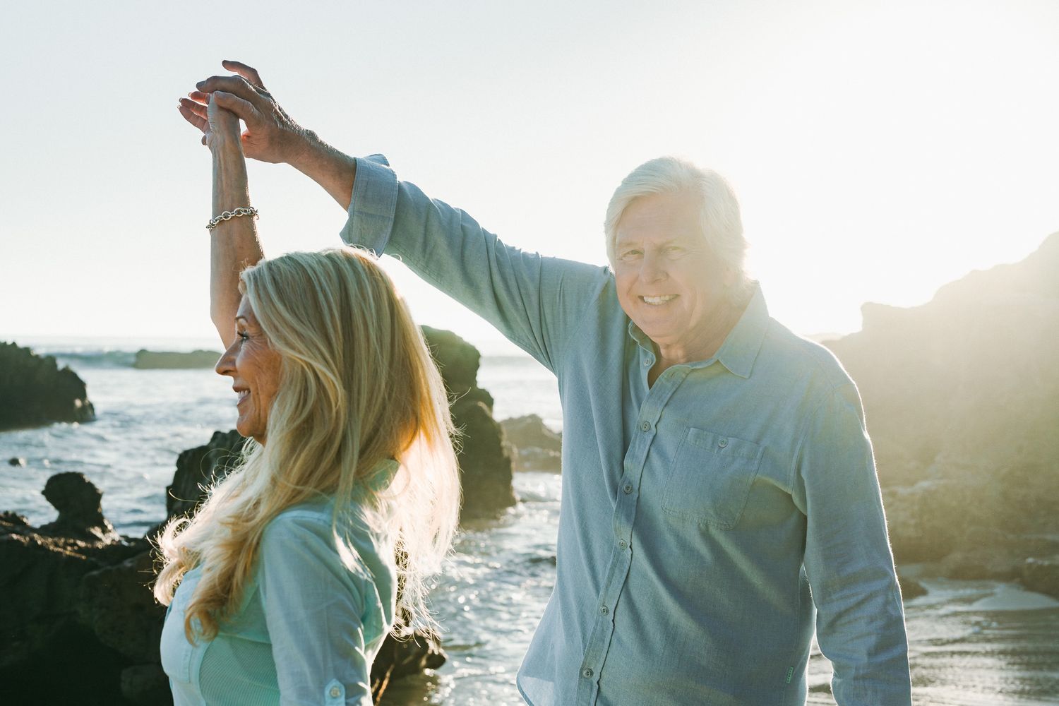 Couple enjoys a romantic sunset moment together on a rocky beach with ocean waves crashing in the background.