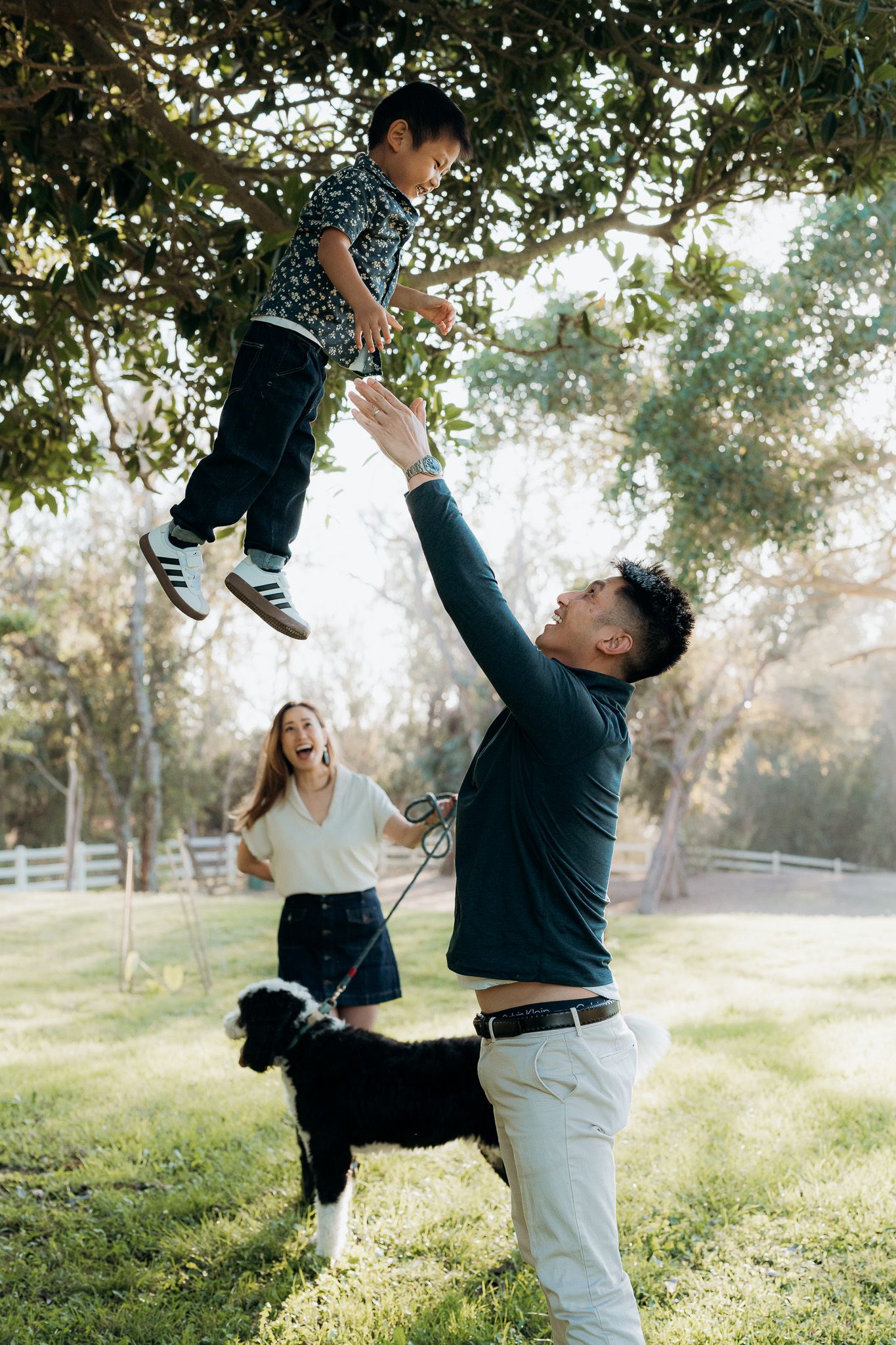 Playful couple dancing and spinning together in a sunlit park with trees and white fencing in the background.