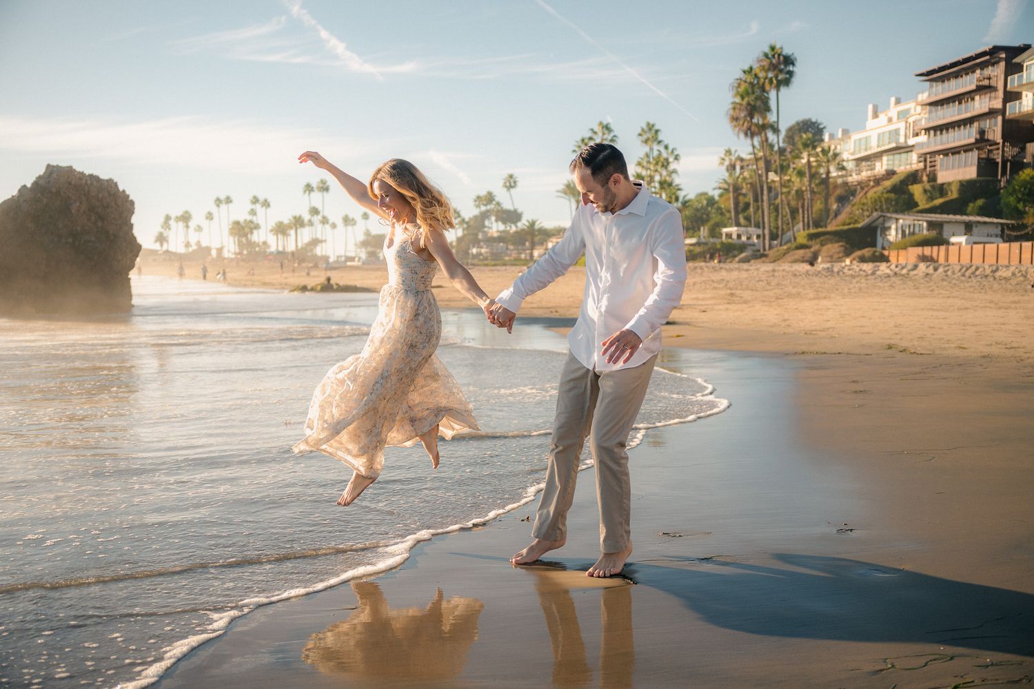 Couple in white outfits sharing a romantic moment on a misty beach at sunset.