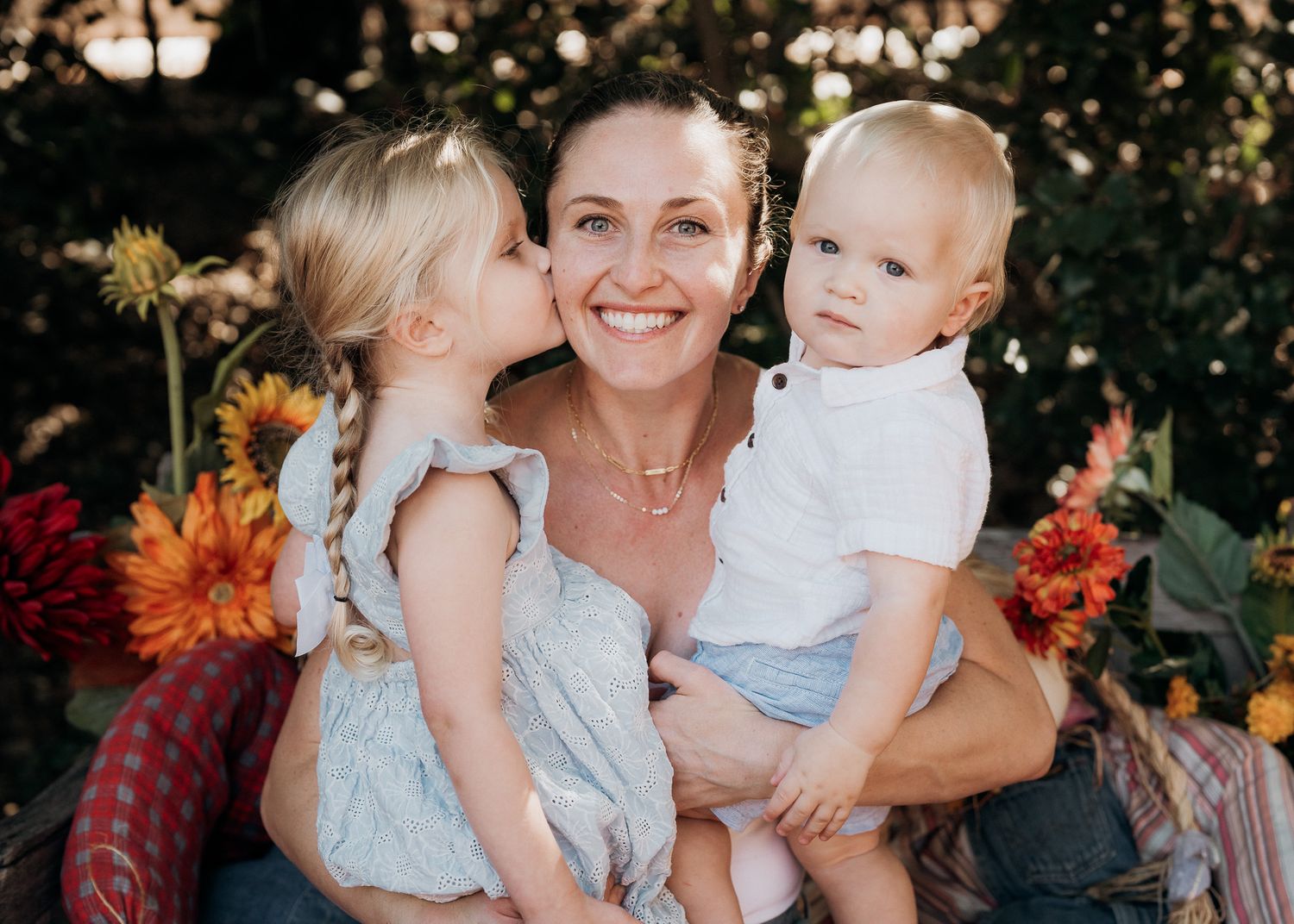 A family poses outdoors in casual clothing surrounded by autumn flowers and natural scenery.