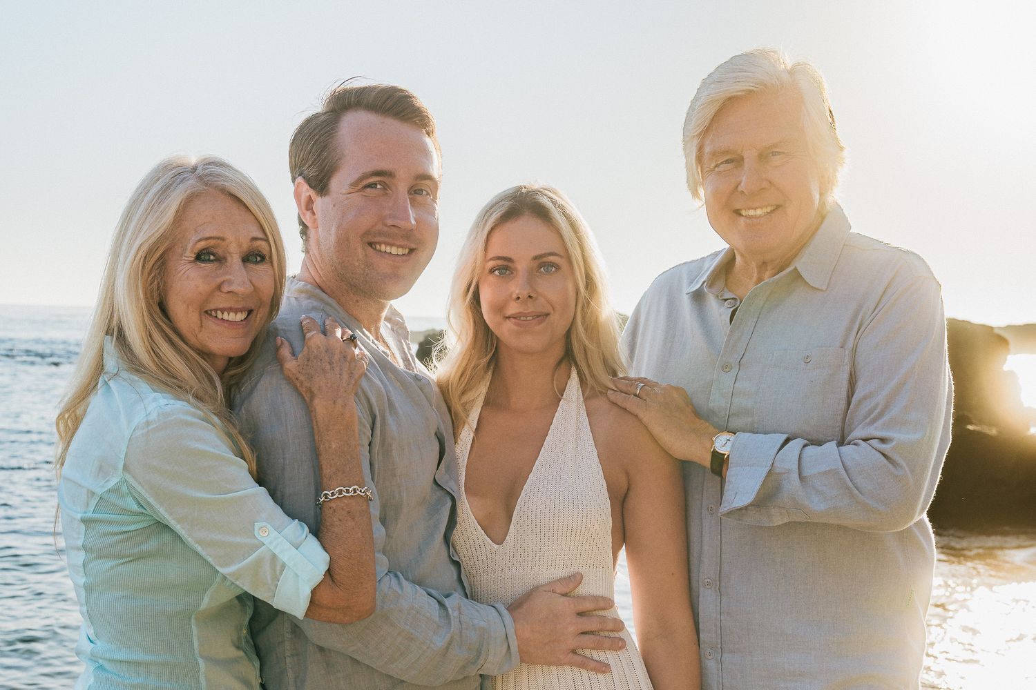 A group of people smiling and laughing together on a beach at sunset.