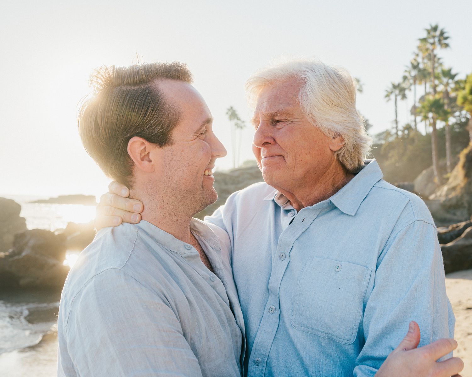 A tender moment between an elderly couple sharing laughter and affection on a sunny beach.