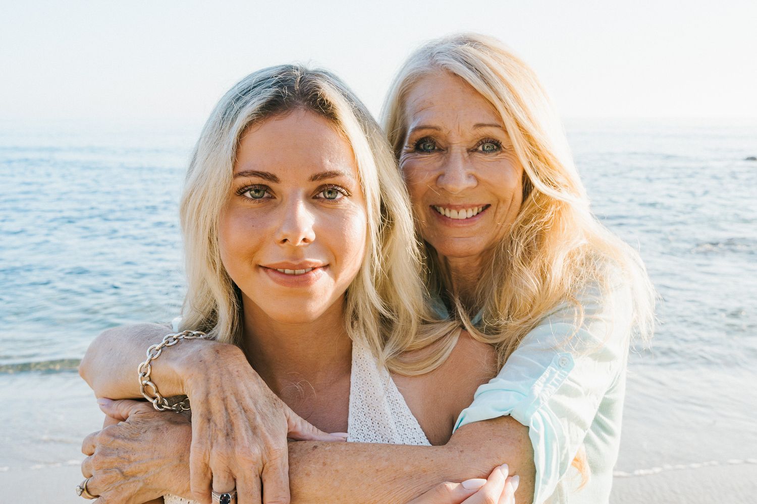 Two blonde women pose together at the beach in a collage of five similar photos at sunset.