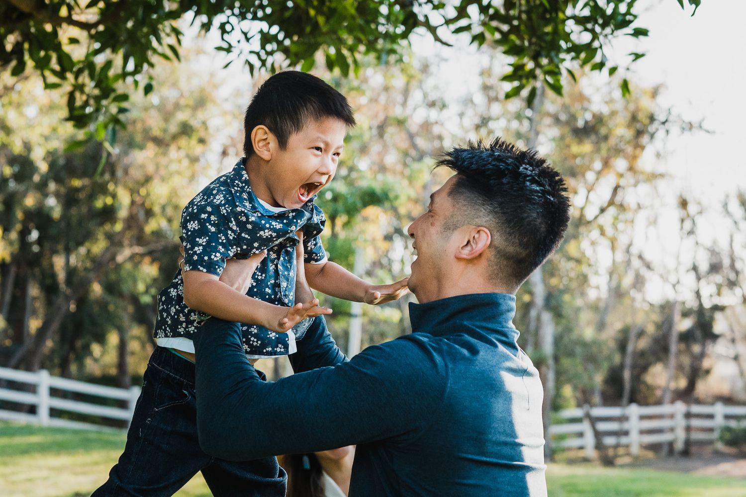 A parent and child share a tender moment while playing together outdoors in a park setting during golden hour.