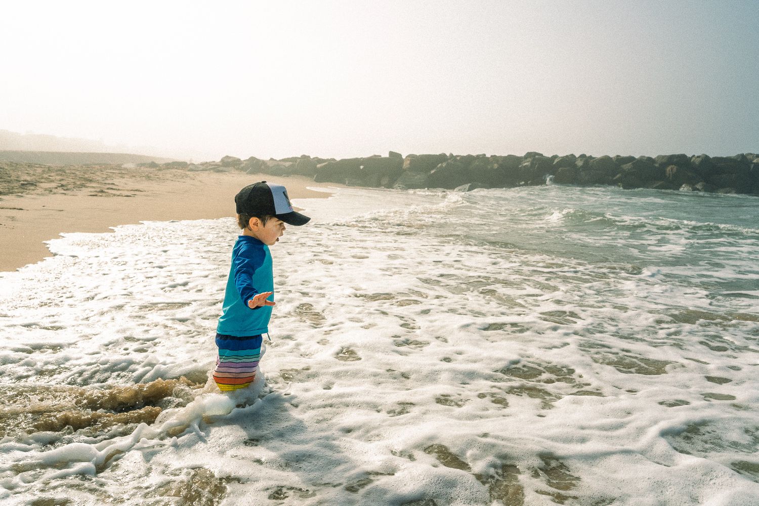 A boy experiencing a small ocean wave covering his feet for the first time.