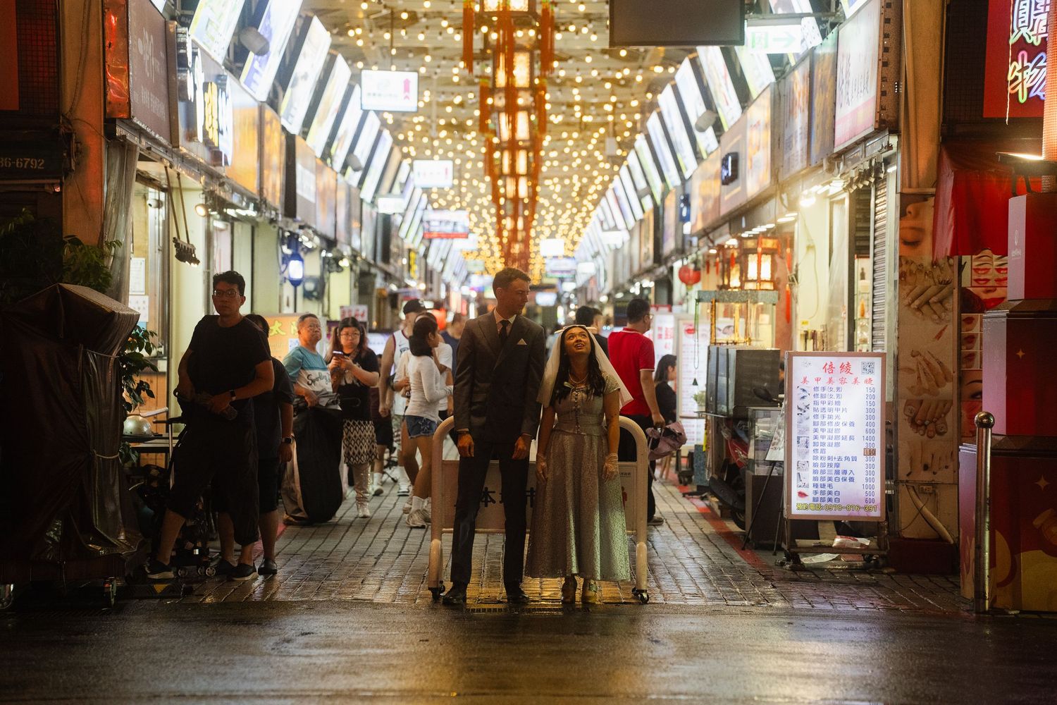 Couple exploring the lively Huaxi Street Night Market in Taipei at night in wedding attire.