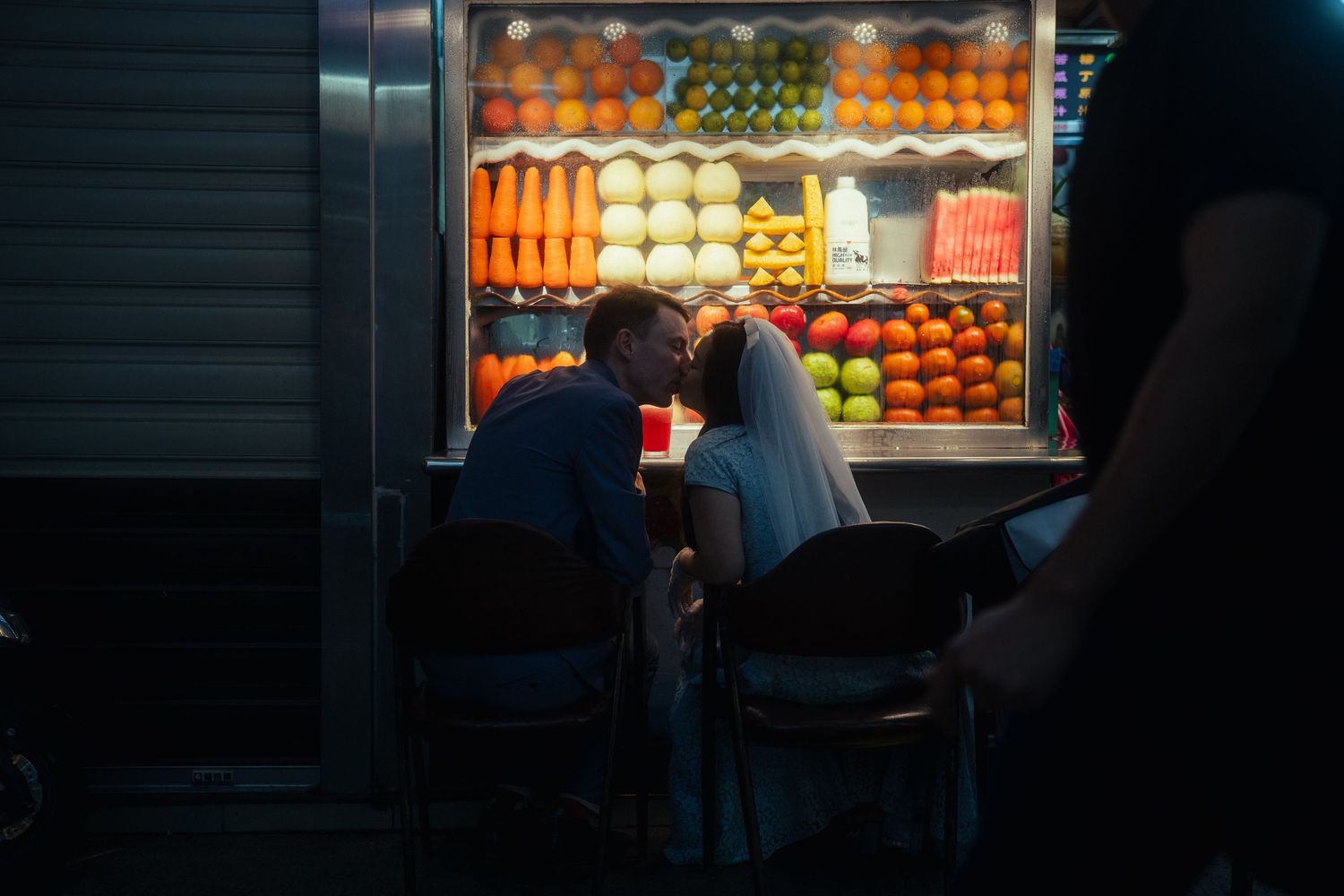 Jolene and Conor kissing beside a colorful fruit stand during their Taipei pre-wedding photoshoot at Huaxi Street Night Market.