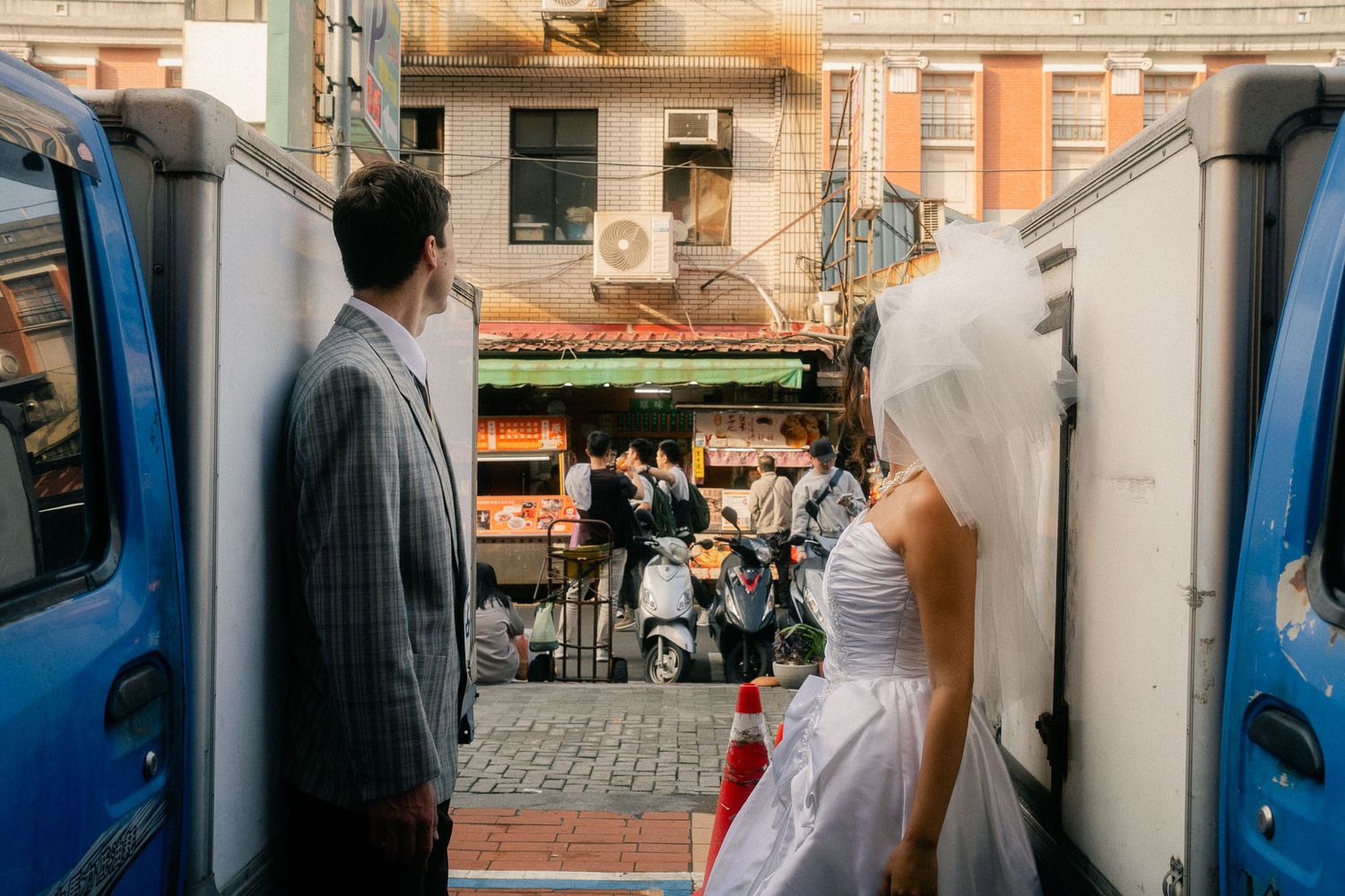 Bride and groom framed between blue delivery trucks during a cinematic Taipei pre-wedding session