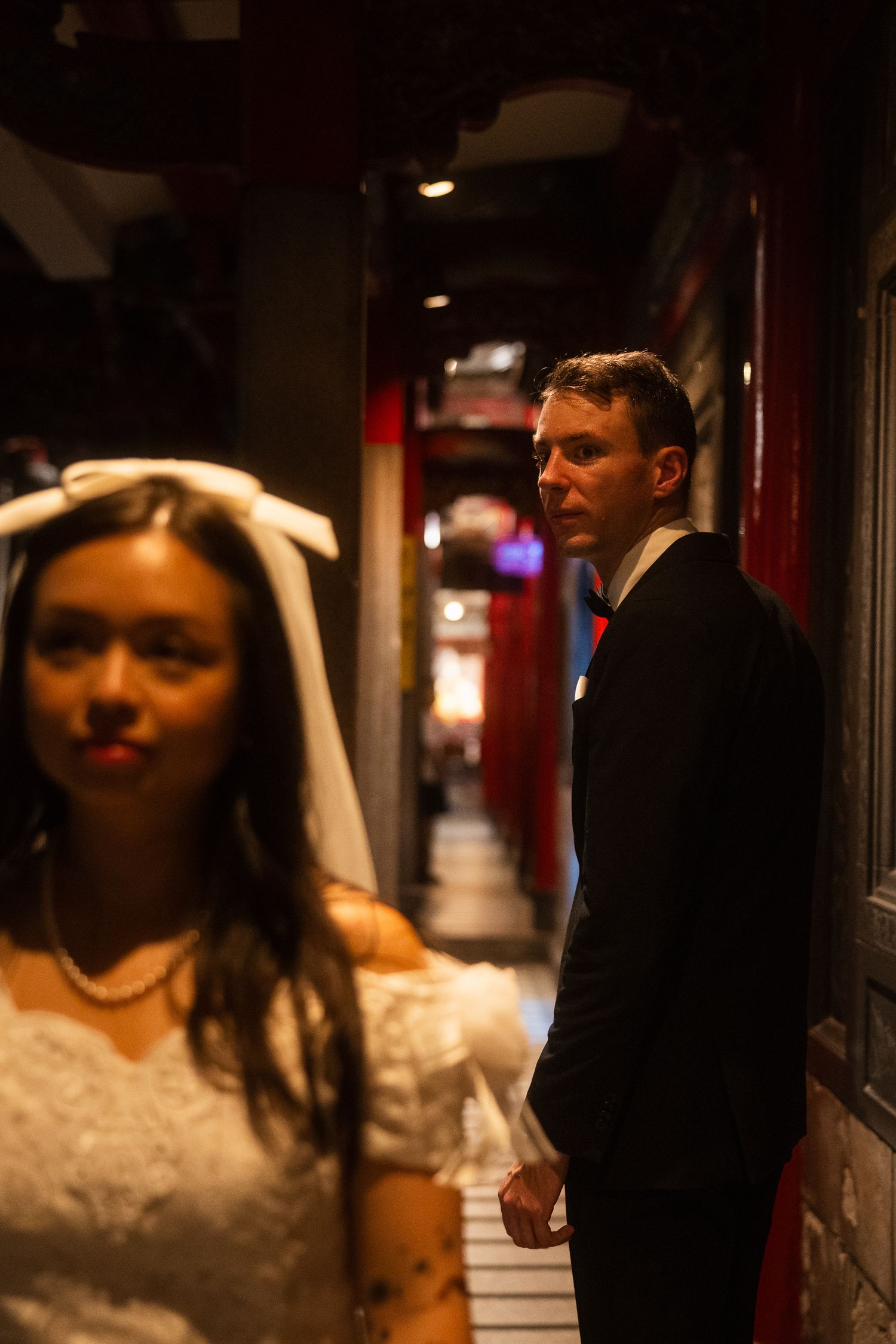 Bride in the foreground with groom looking back inside a traditional Taipei temple at night