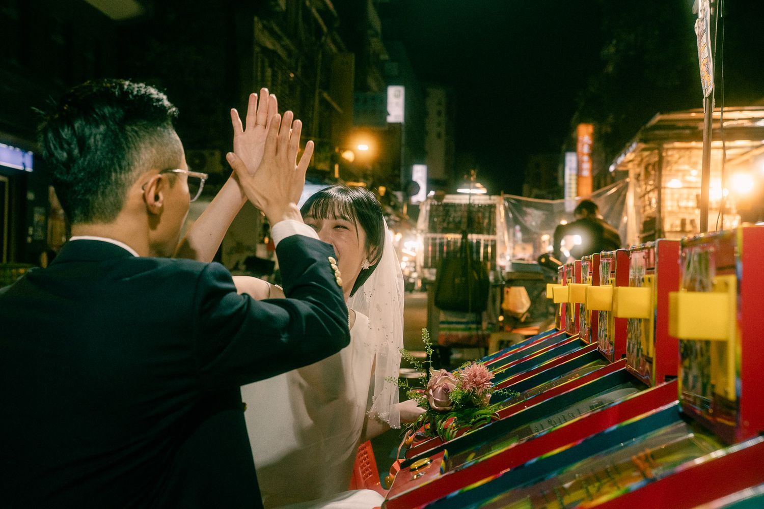 Bride laughing with her groom beside colorful arcade machines during a playful Taipei pre-wedding photoshoot