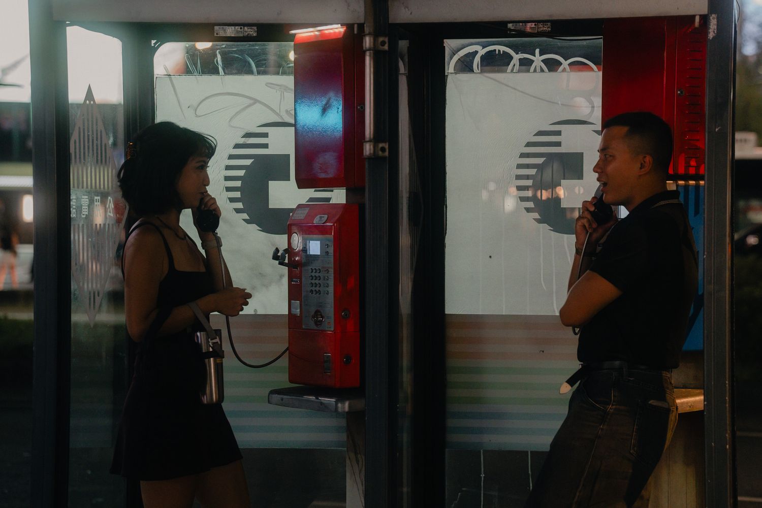 Couple talking on vintage public phones during a cinematic night photoshoot in Ximending, Taipei