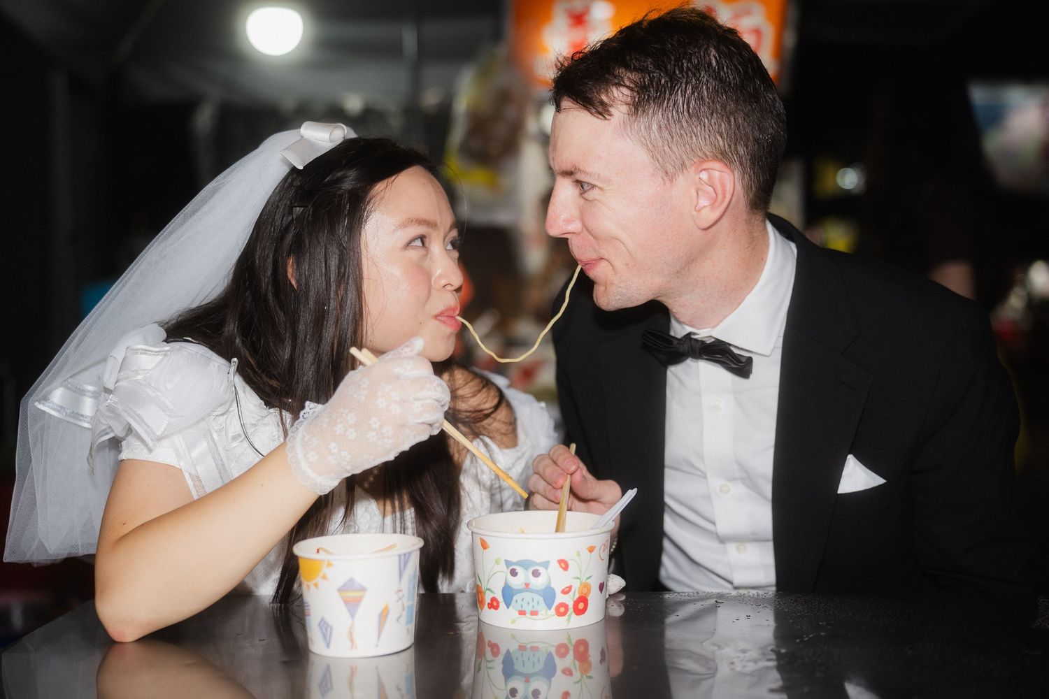 Bride and groom sharing a noodle while eating at a local Taipei street food stall
