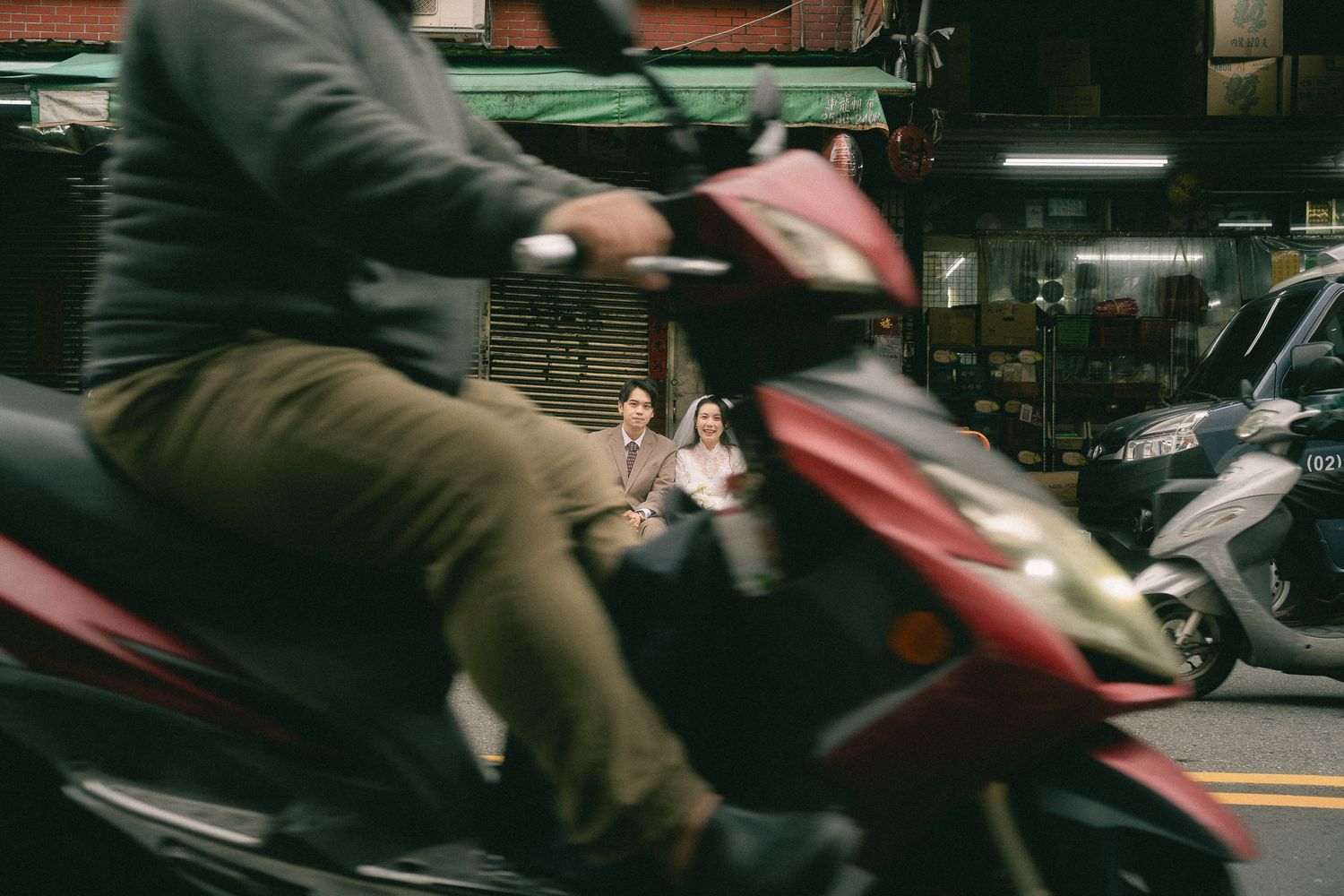 Passing scooter frames a bride and groom during a documentary-style Dihua Street pre-wedding shoot in Taipei