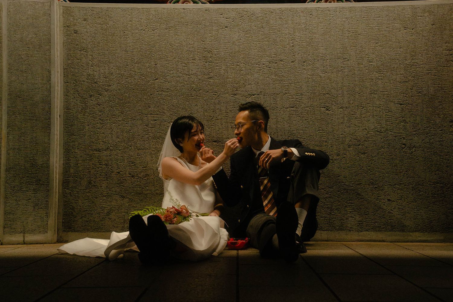 Bride and groom sitting together and eating strawberries near Longshan Temple after their Huaxi Street Night Market photoshoot