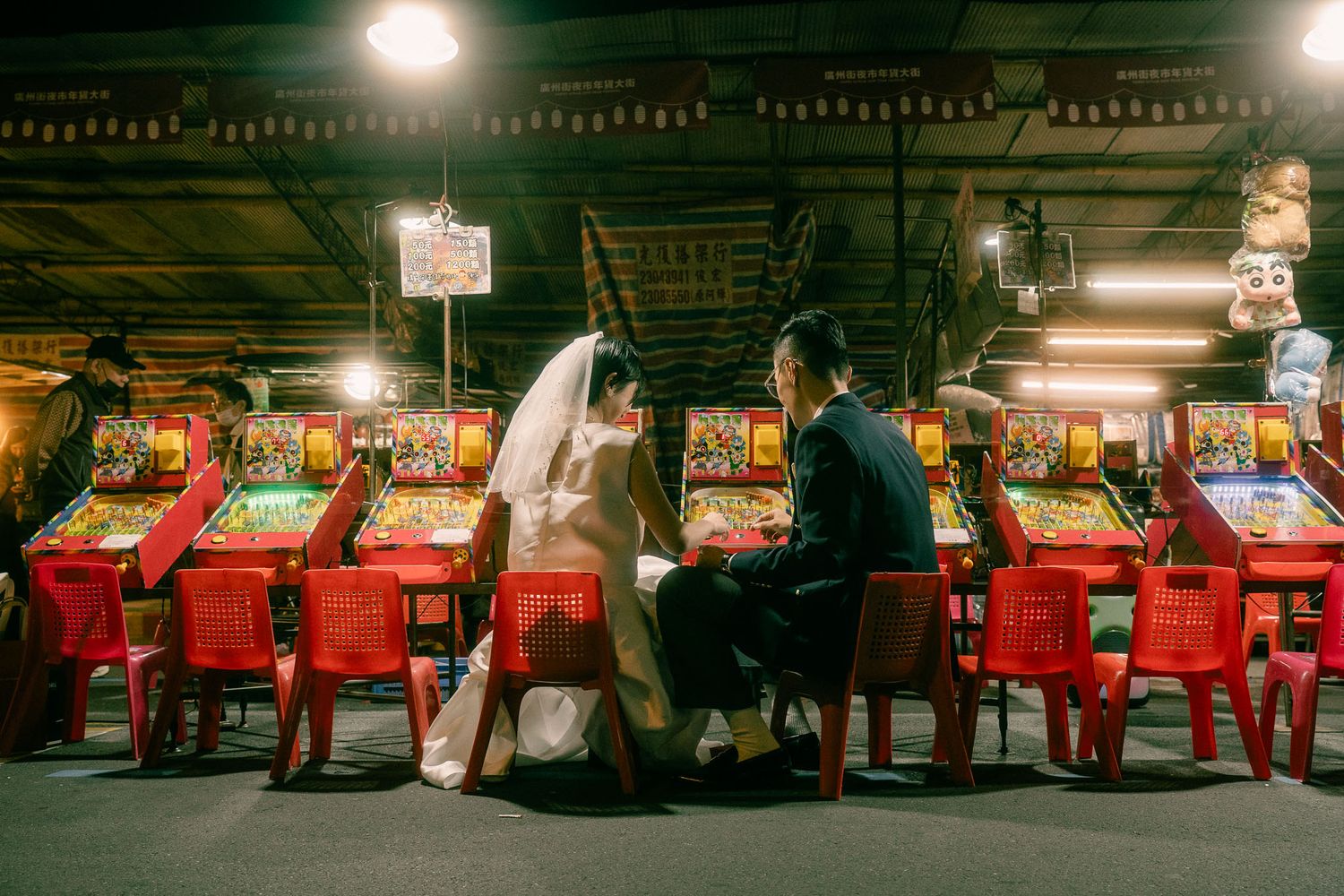 Taiwan pre wedding photography of a bride and groom playing arcade games at a traditional Taipei Huaxi Street night market.