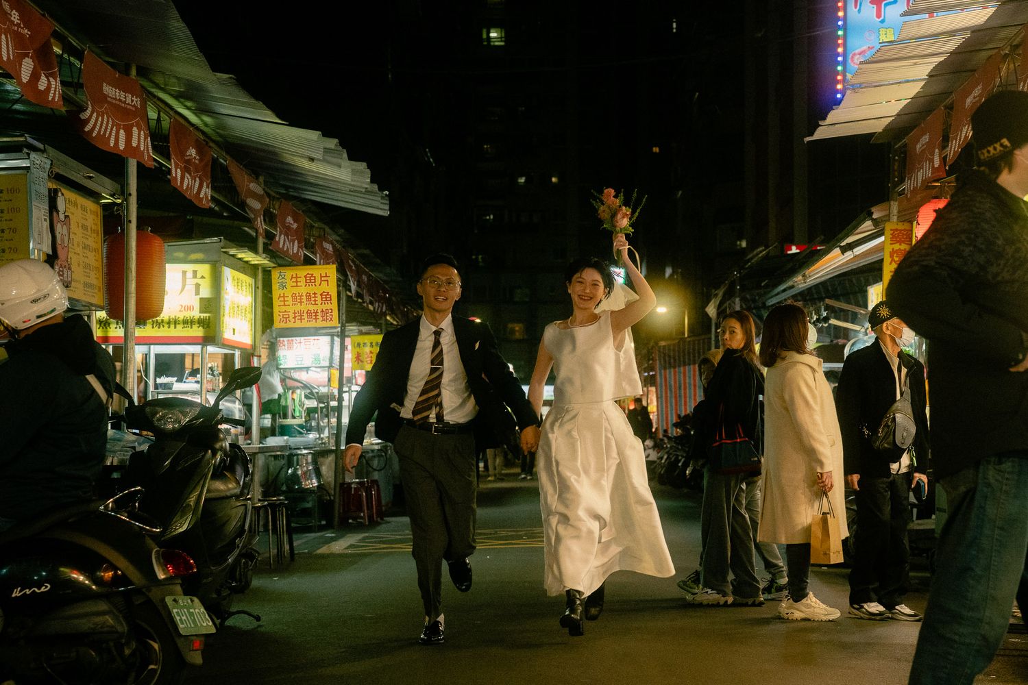 Cinematic Taipei pre-wedding photo of a bride and groom running through a busy night market street