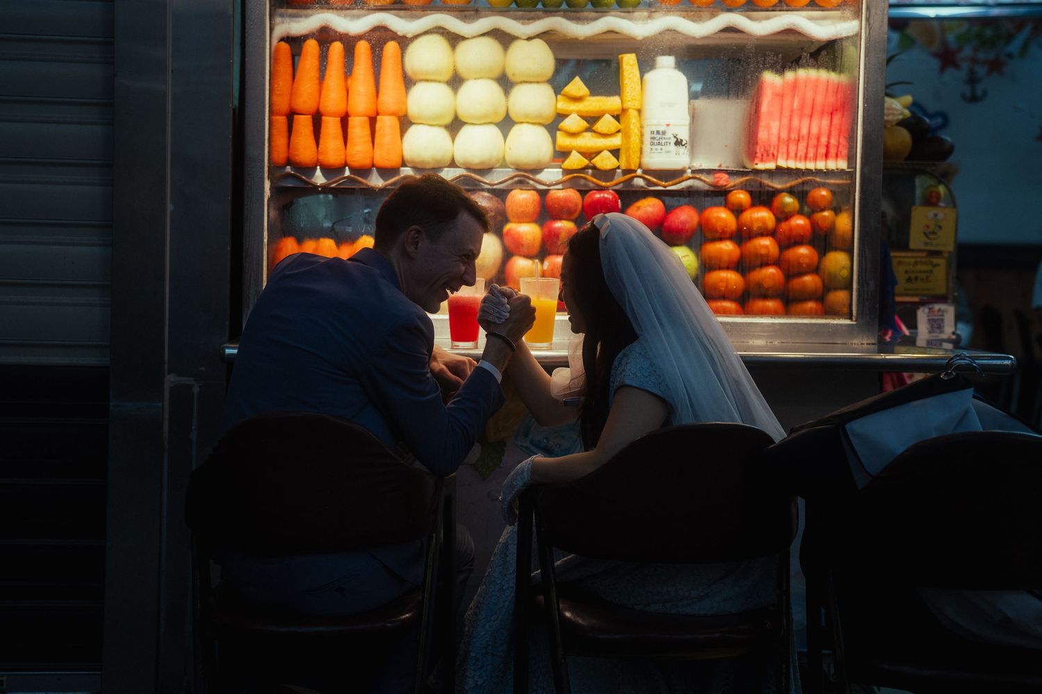 Couple arm wrestling at a colorful fruit juice stand during their Taipei pre-wedding photoshoot