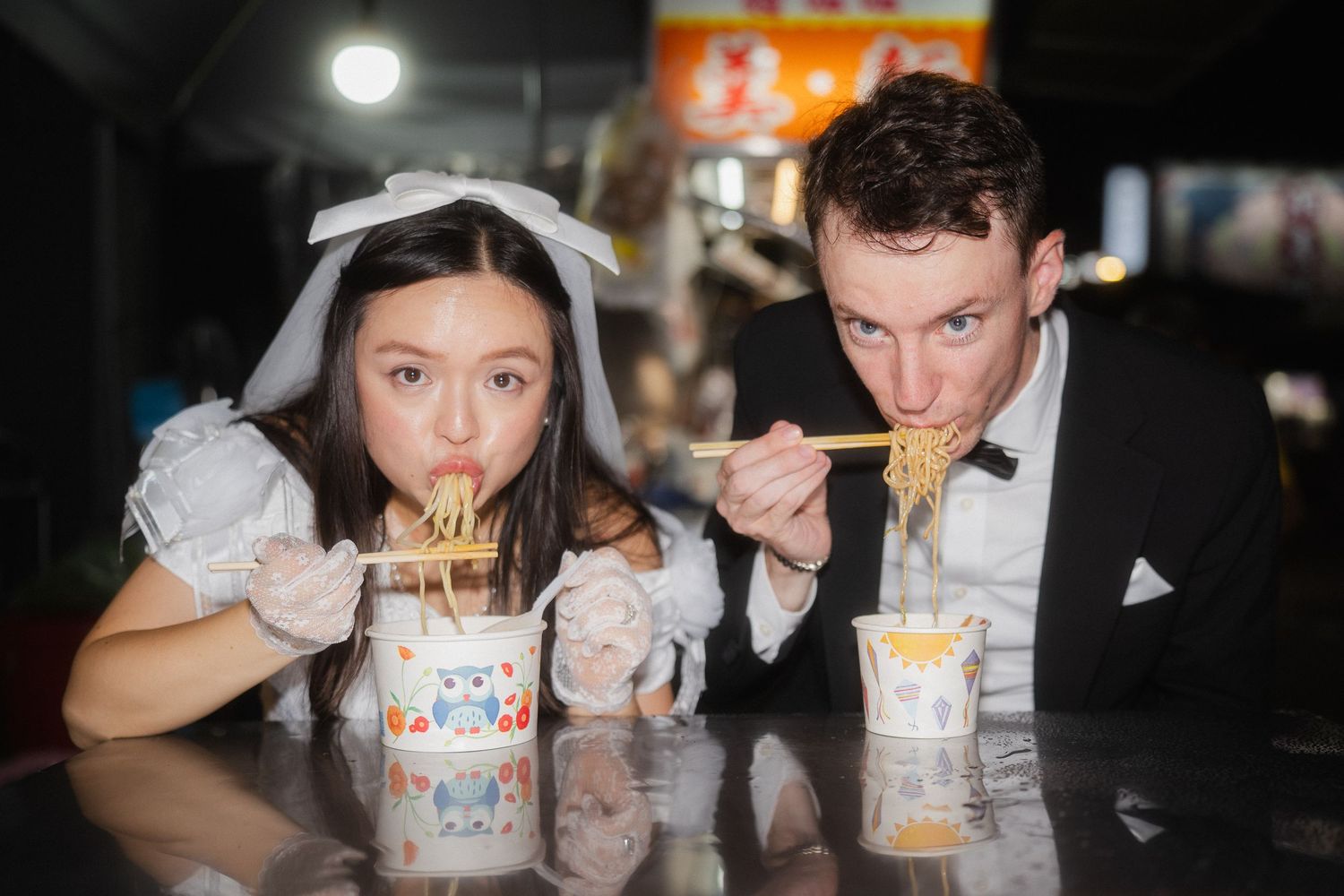 Bride and groom eating noodles together with direct flash during a playful Taipei night pre-wedding photoshoot