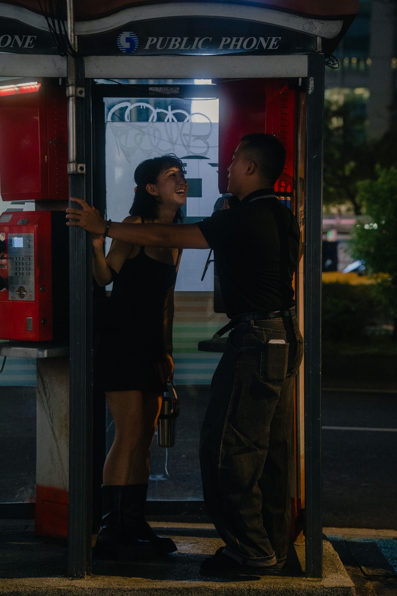 Couple laughing together inside an old public phone booth during their Ximending couple photoshoot in Taipei