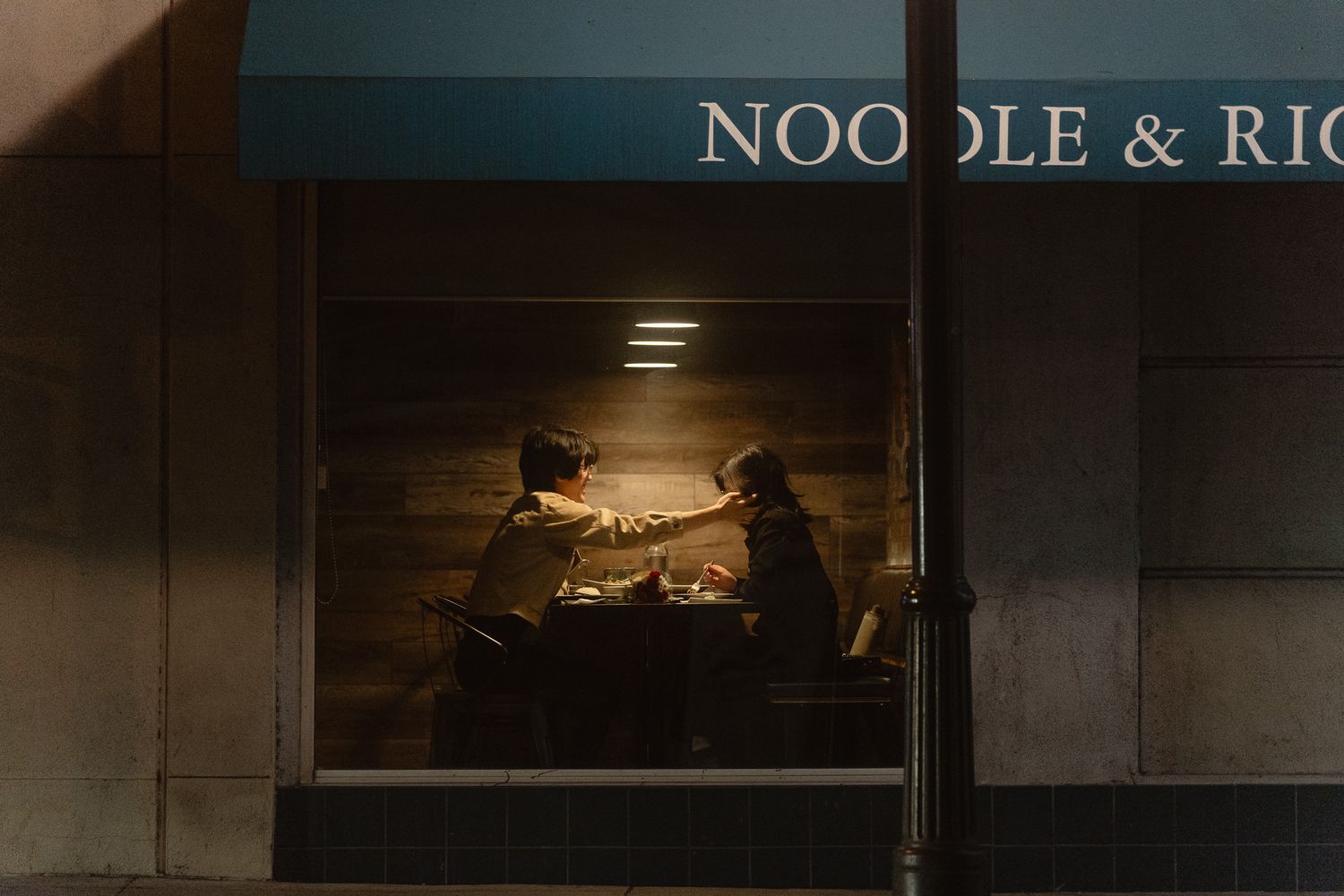 Cinematic Taipei date night photography of a couple seen through a warm restaurant window