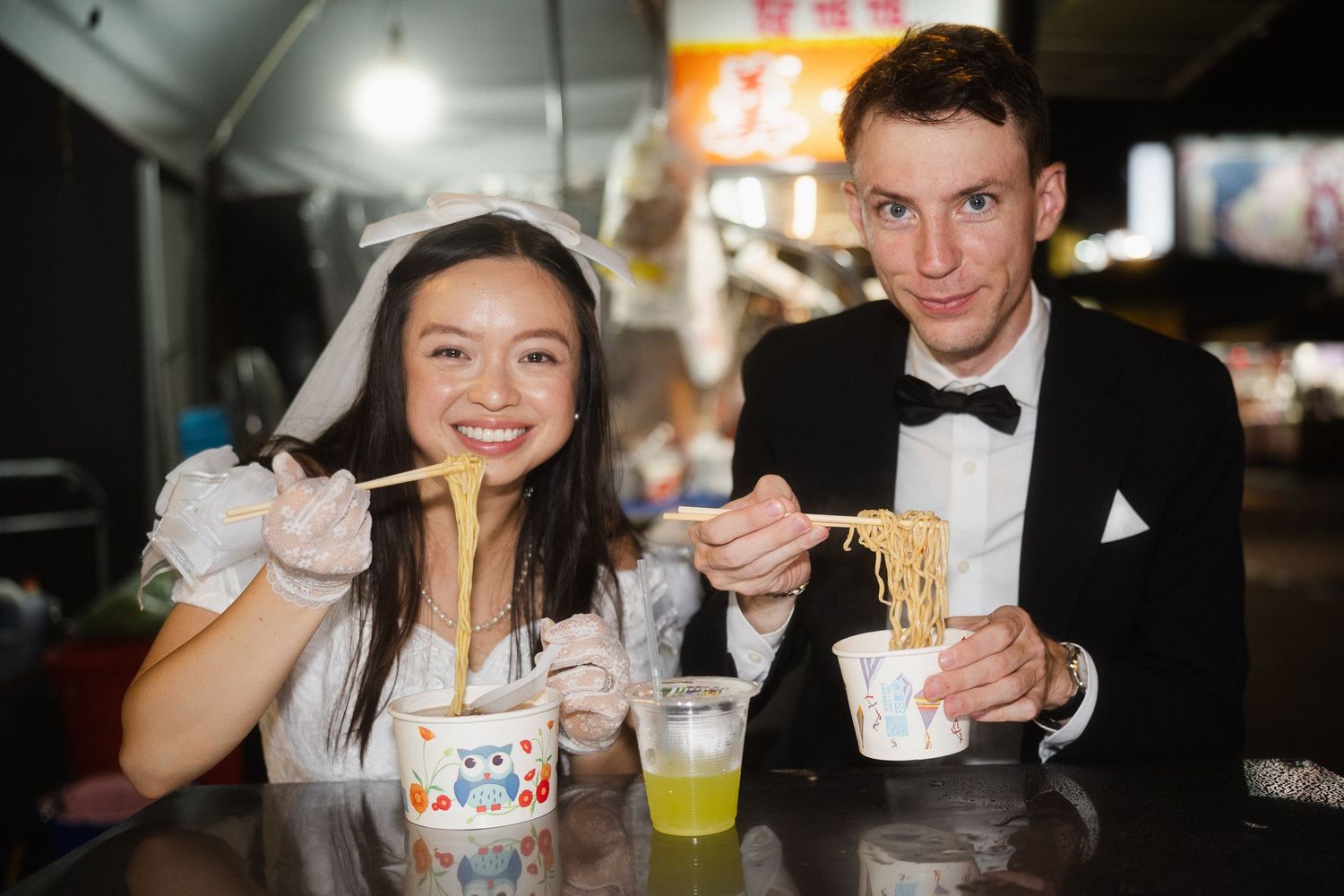 Bride and groom eating noodles together during a candid pre-wedding photoshoot at Huaxi Street Night Market in Taipei.