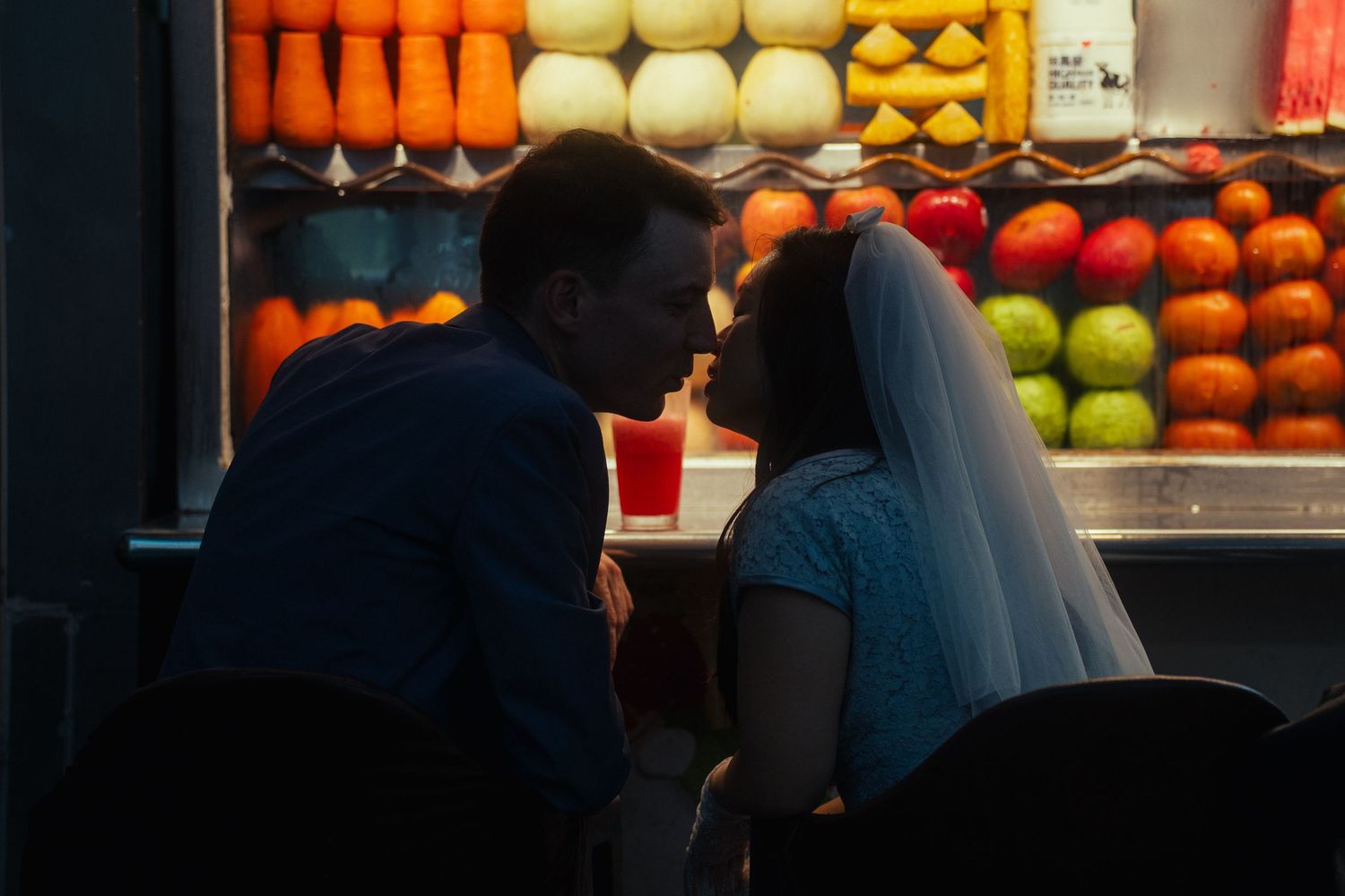 Bride and groom leaning in for a kiss in front of a colorful Taiwanese fruit stand in Taipei