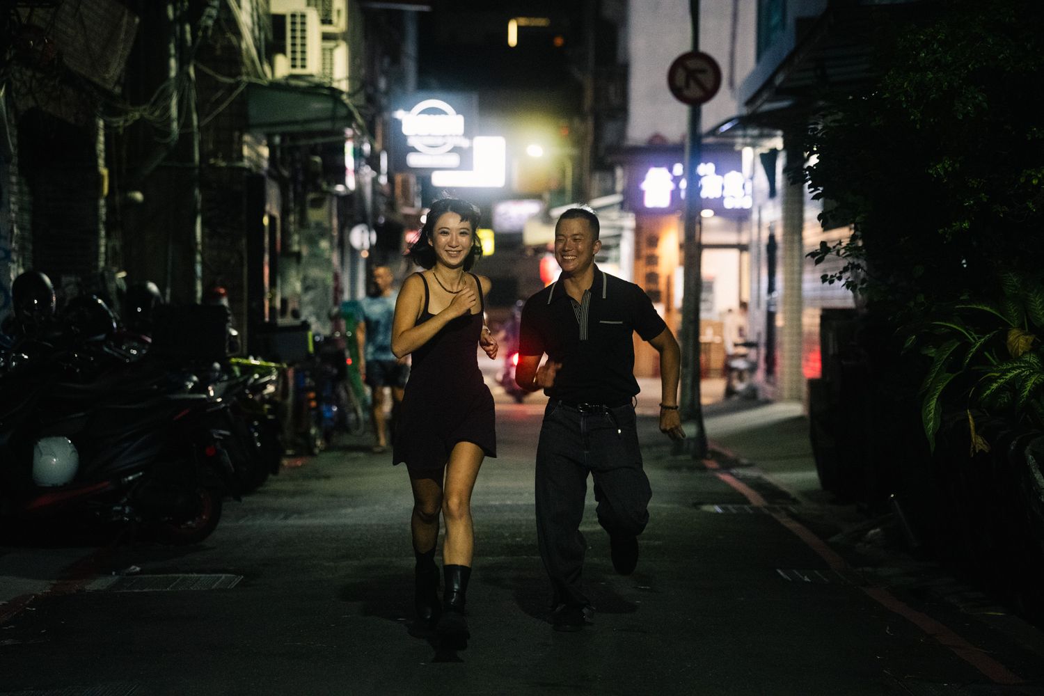 Couple laughing and racing down a Ximending side street during a nighttime Taipei photoshoot