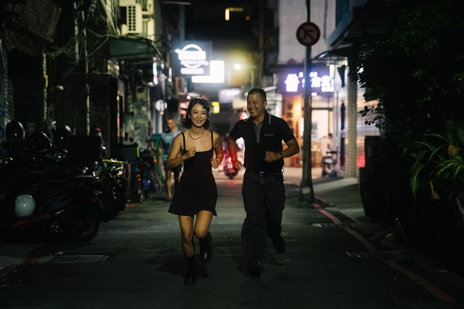 Couple racing down a quiet street at night during a candid Ximending photoshoot in Taipei, Taiwan