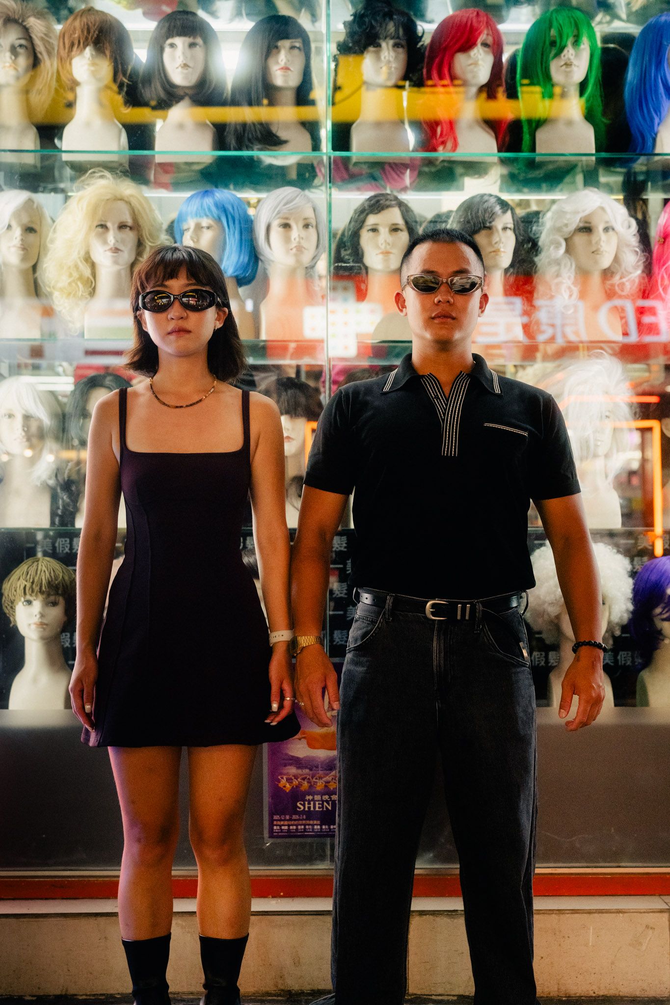 Couple wearing sunglasses in front of colorful mannequin wigs during a creative Ximending photoshoot in Taipei