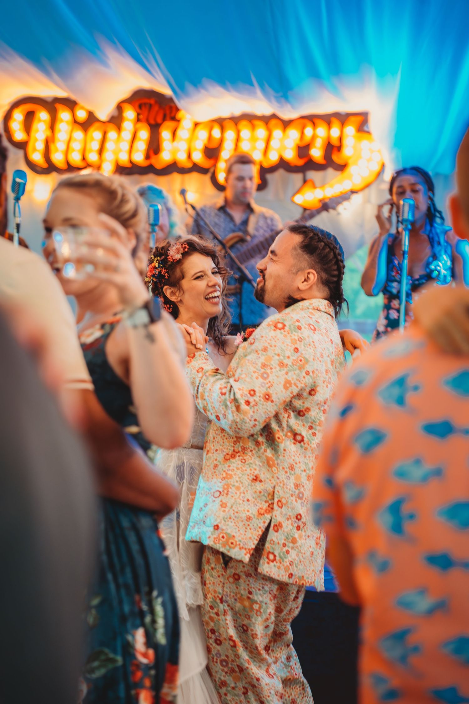 Couple dancing joyfully at a vibrant wedding reception with a live band and neon Highsteppers sign.