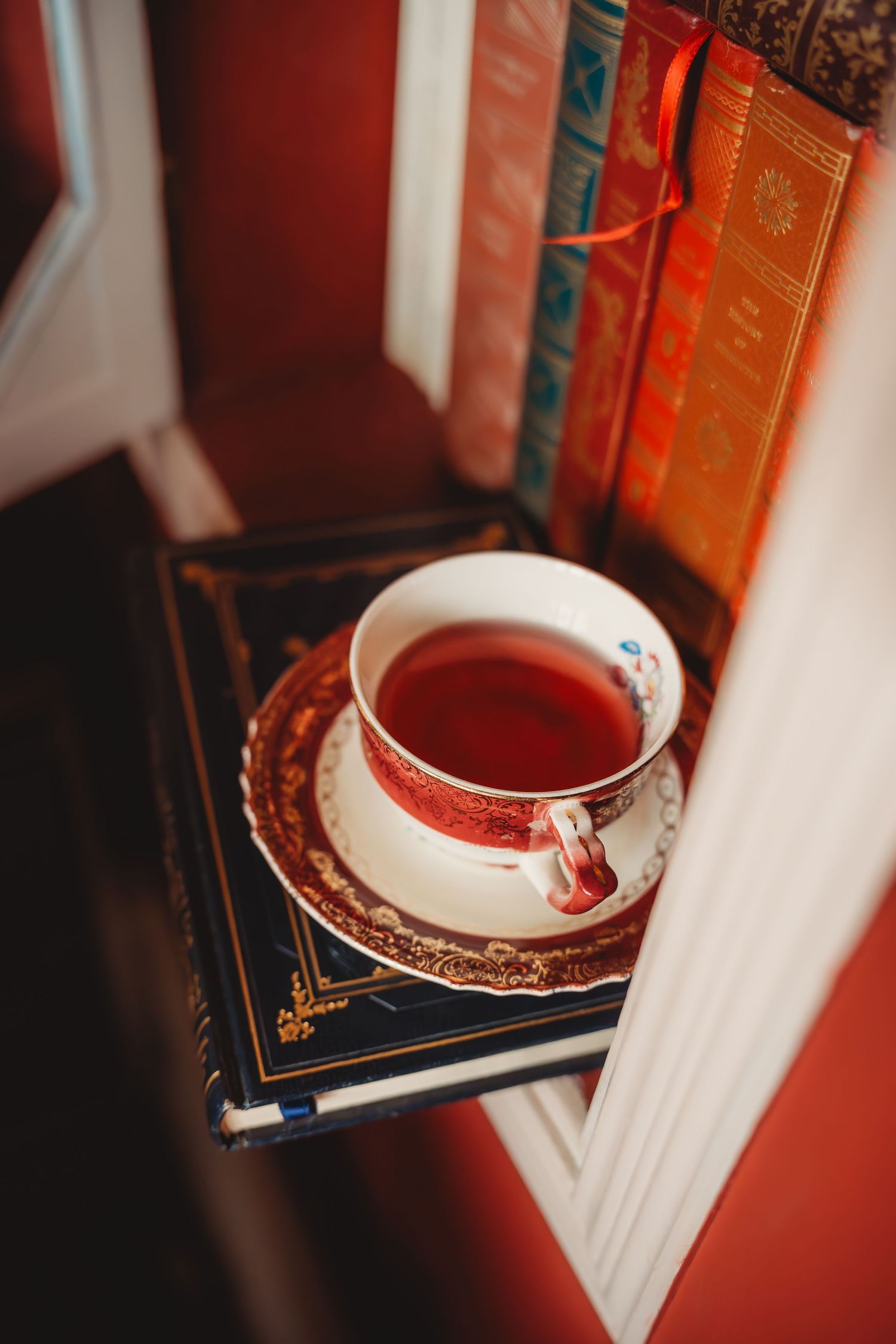 Elegant red and white teacup with saucer resting on vintage books beside a colorful bookshelf.